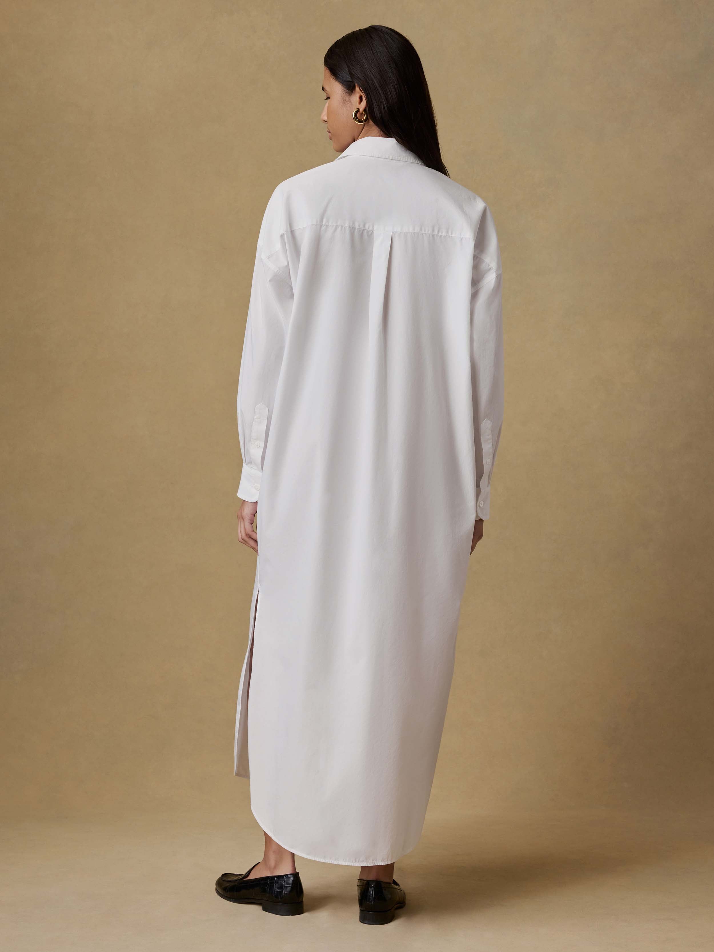 Back view of a woman wearing a long white dress against a beige background