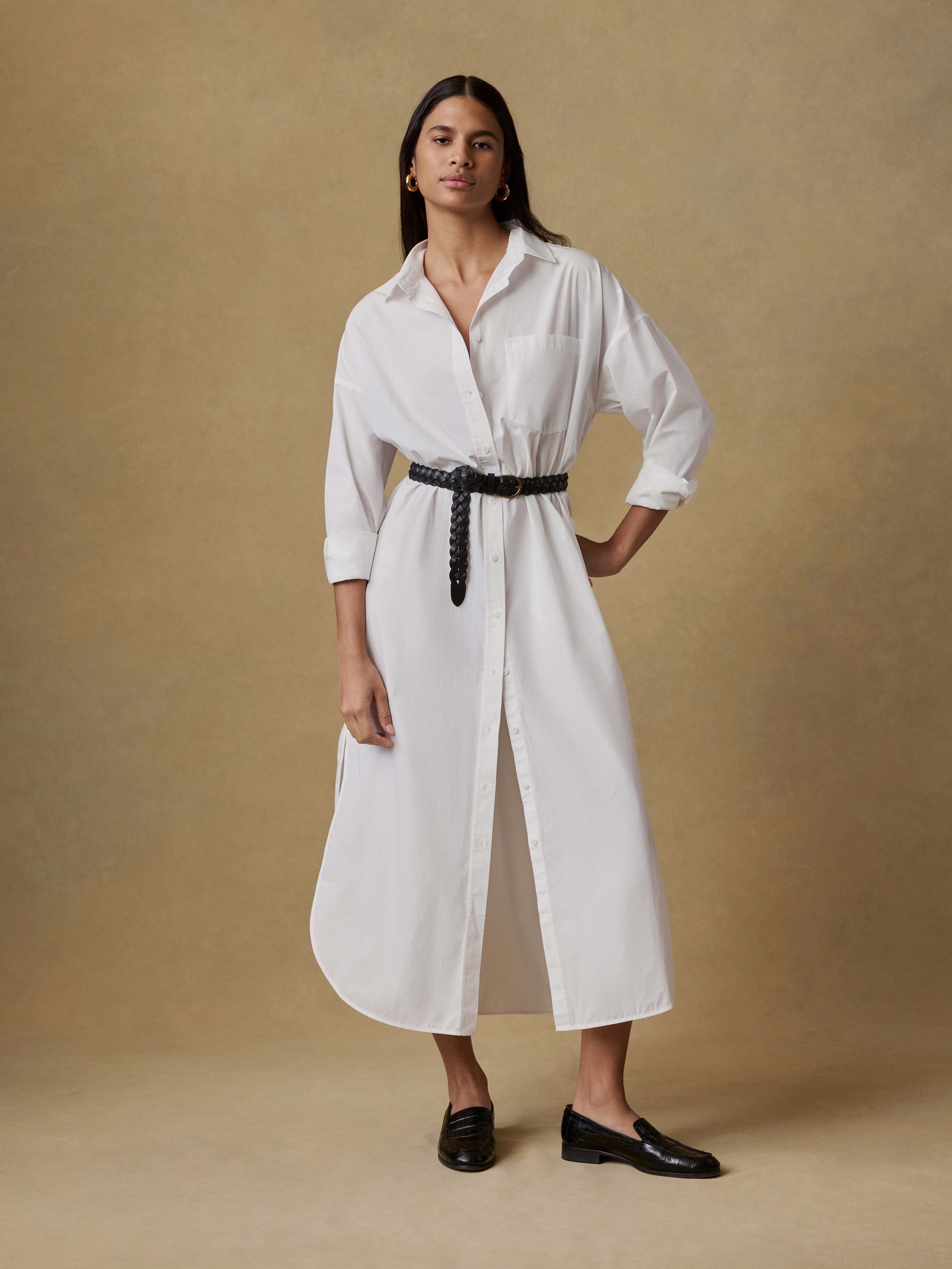 Woman wearing a white dress with a black belt against a beige background