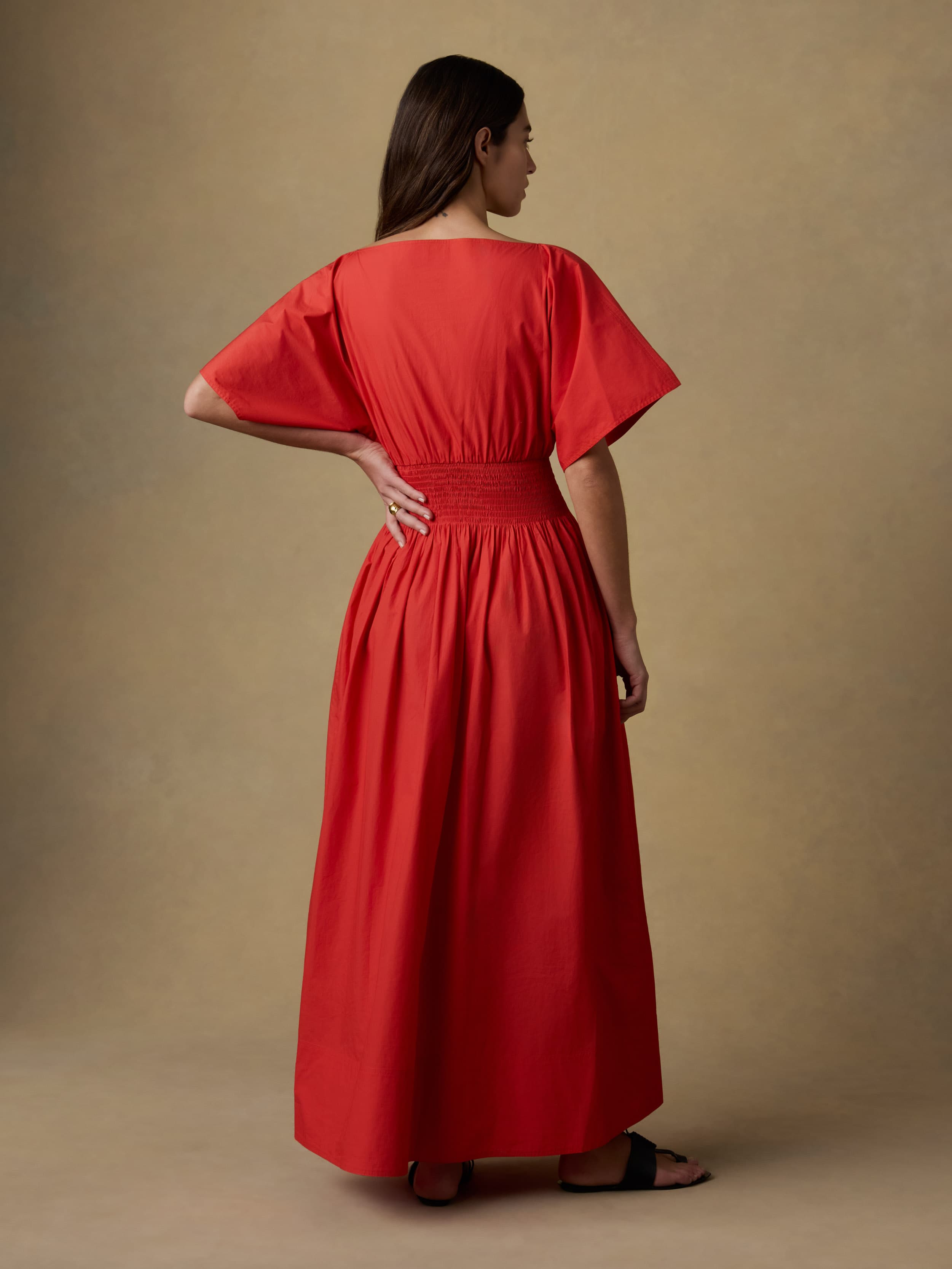 Back view of a woman wearing a red dress against a beige background