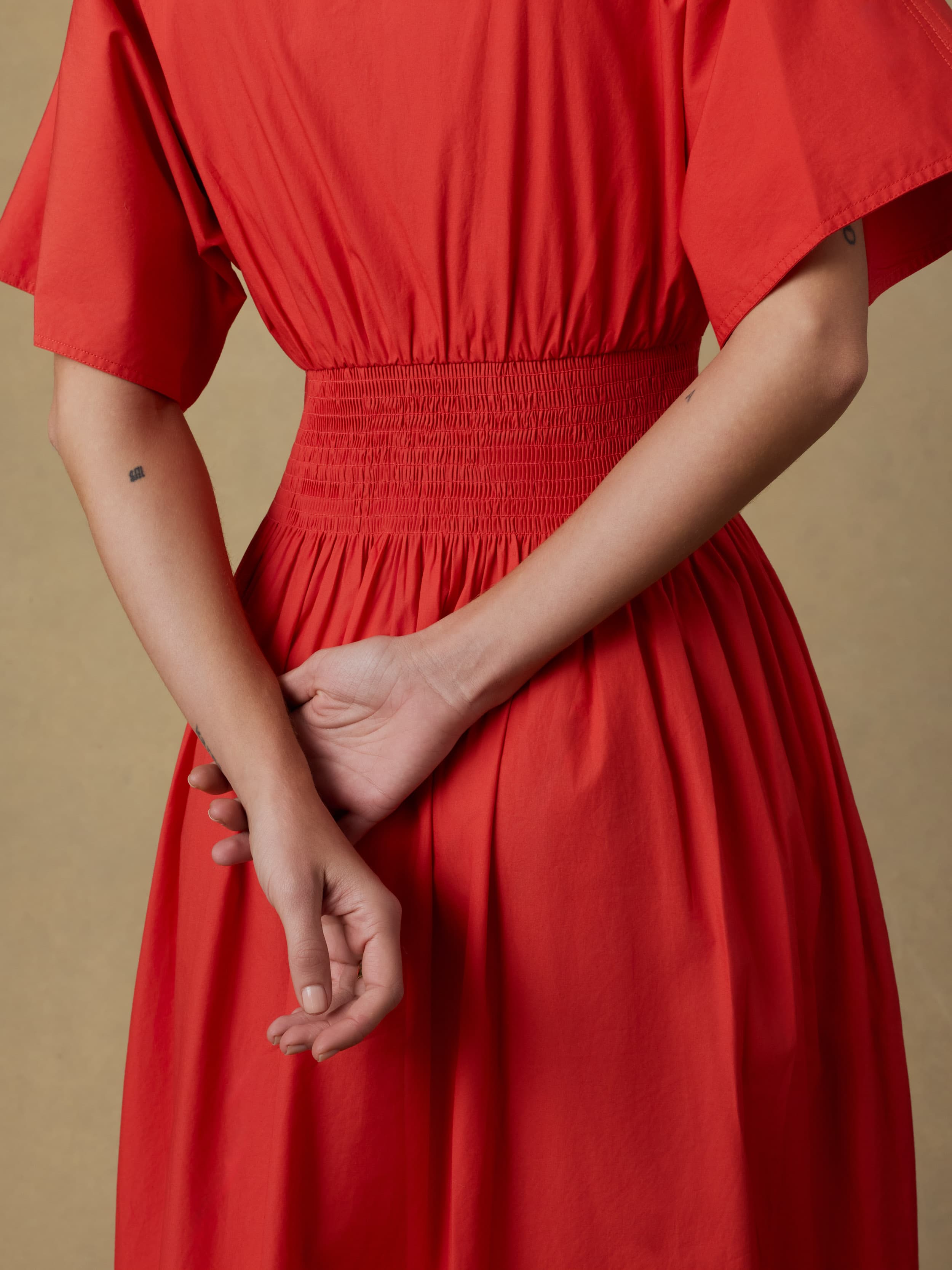 Close up shot of a woman wearing a red dress against a beige background