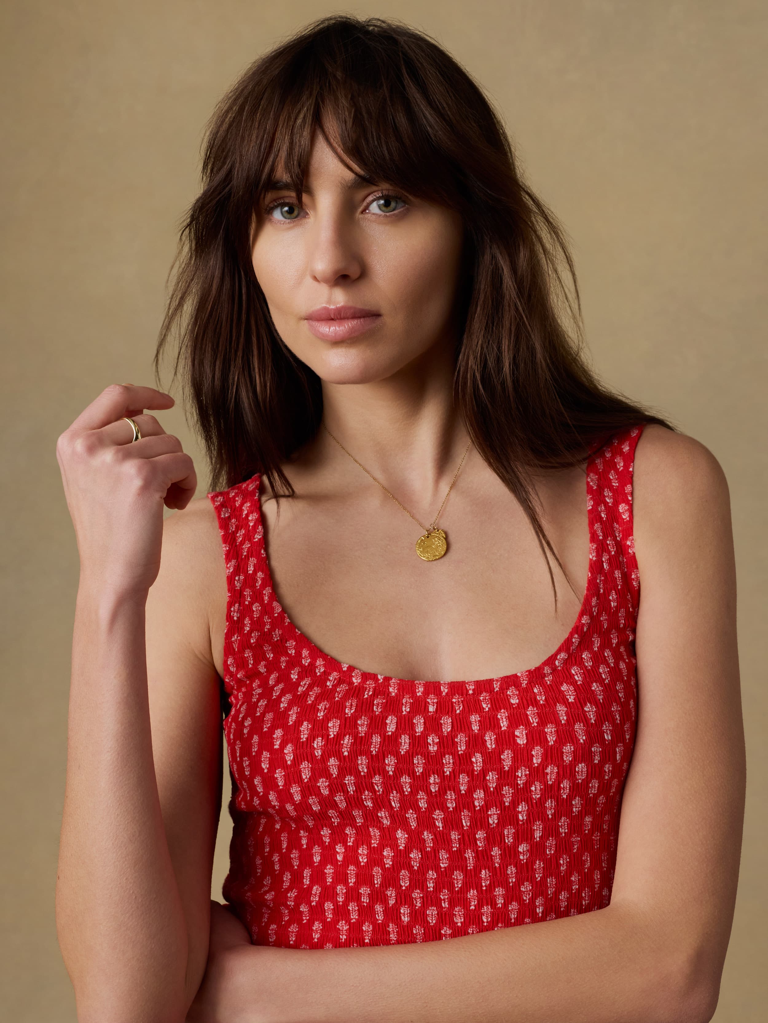 Close up shot of a woman wearing a red floral patterned dress against a beige background
