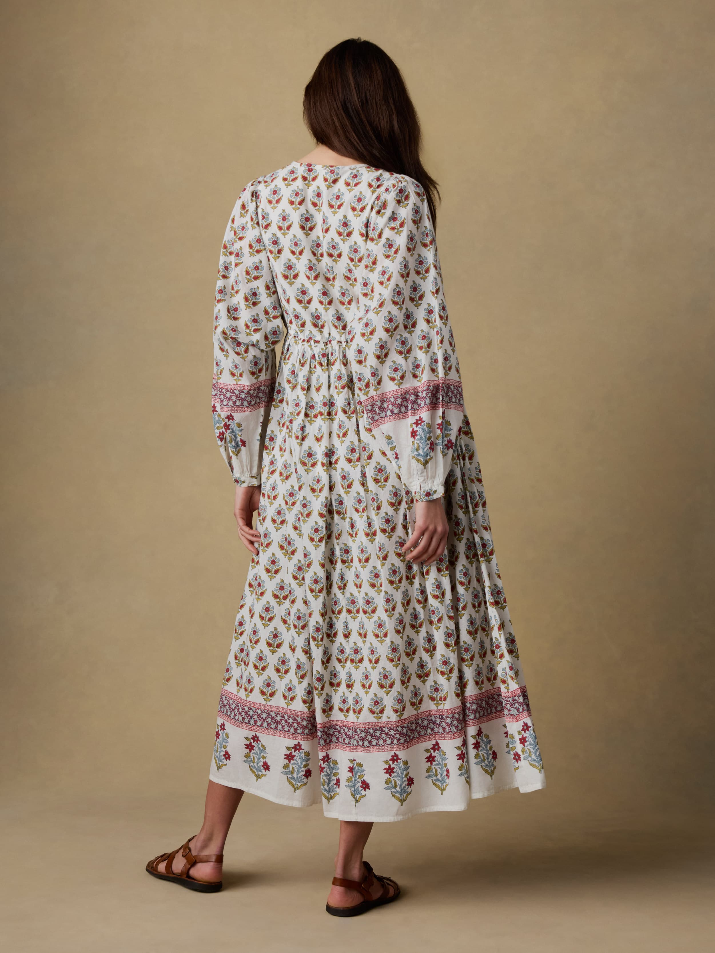 Back view of a woman wearing a long floral dress against a beige background