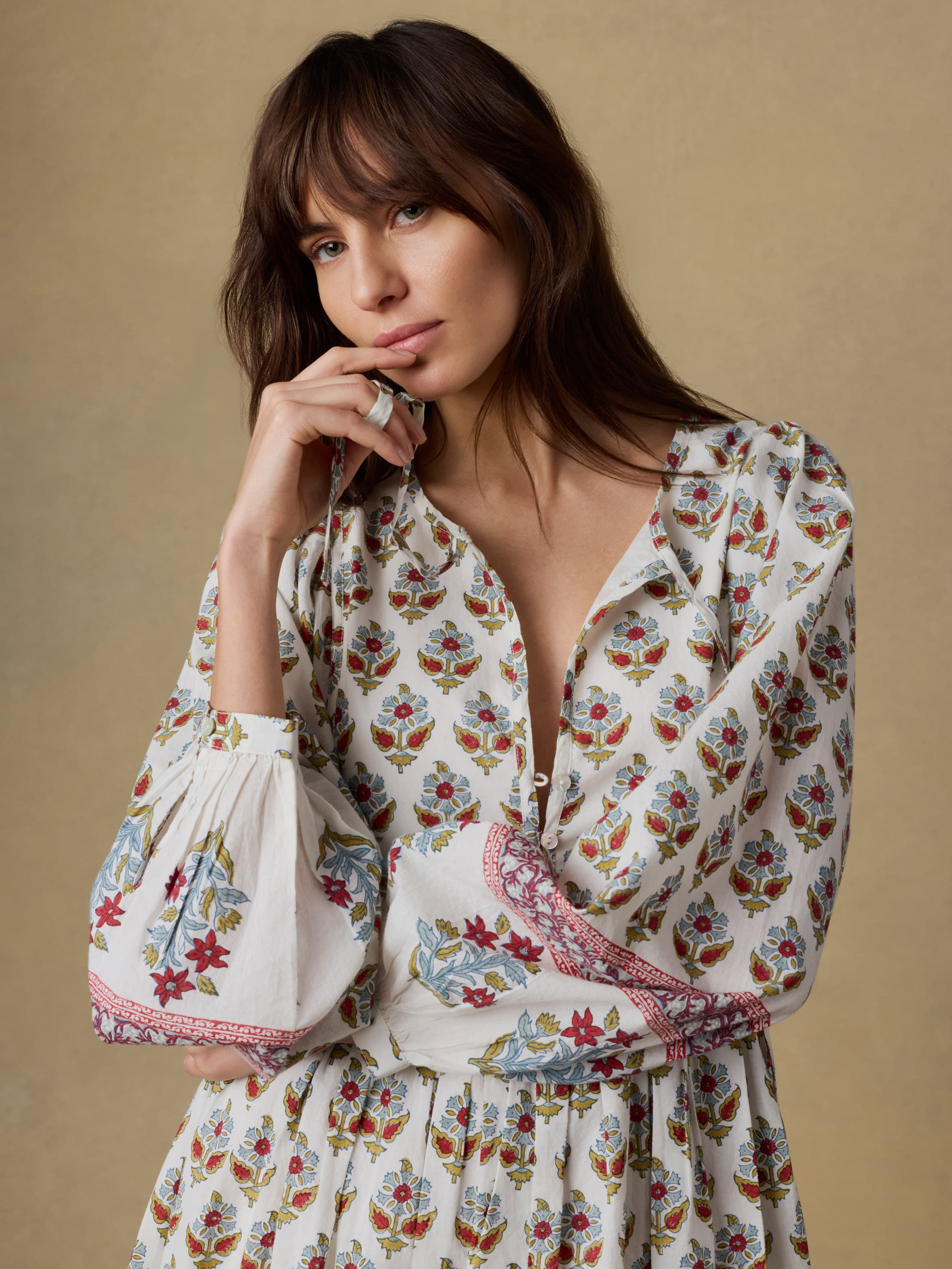 Close up shot of a woman wearing a long floral dress against a beige background