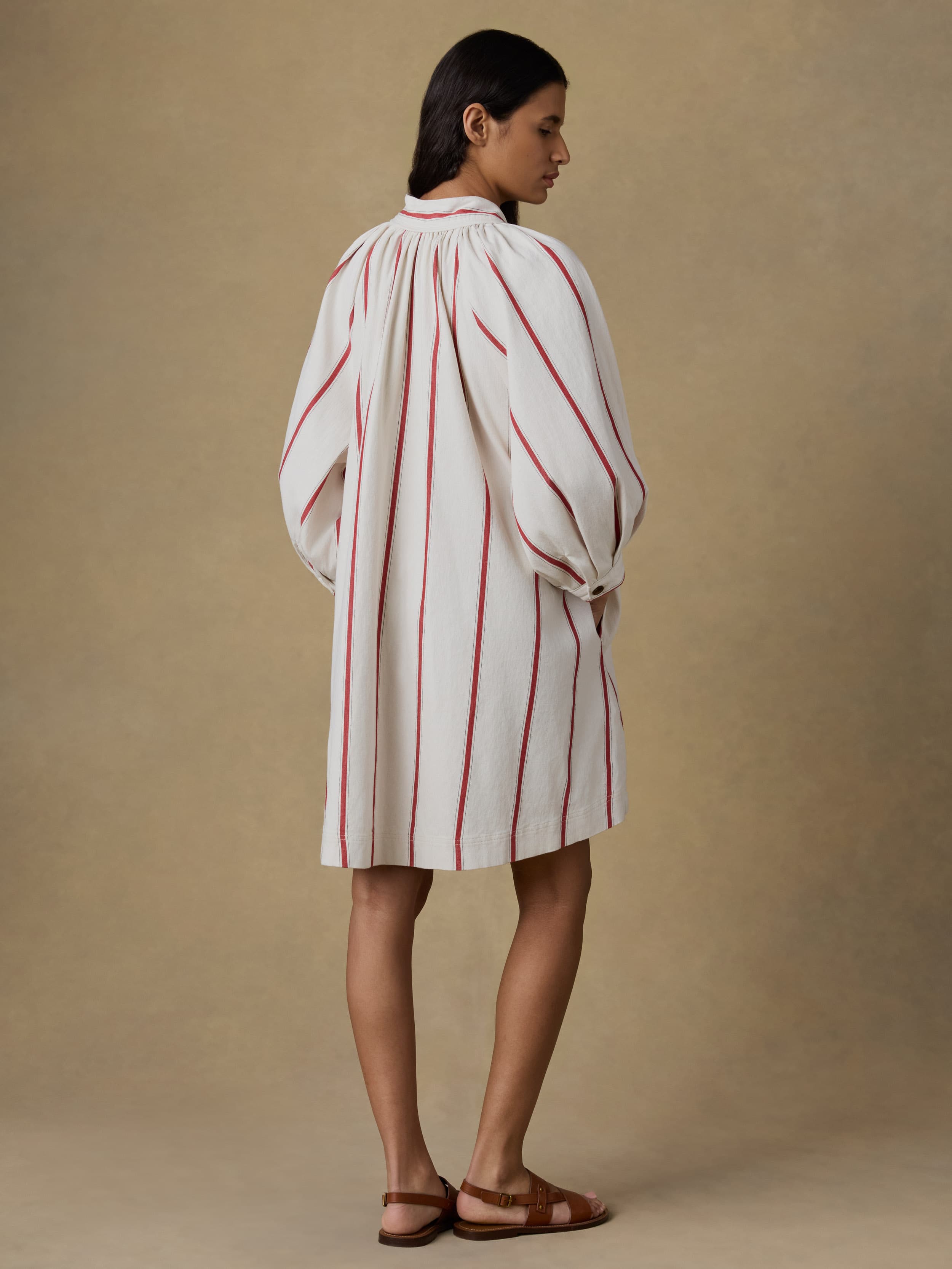 Woman wearing a white dress with red stripes against a beige background