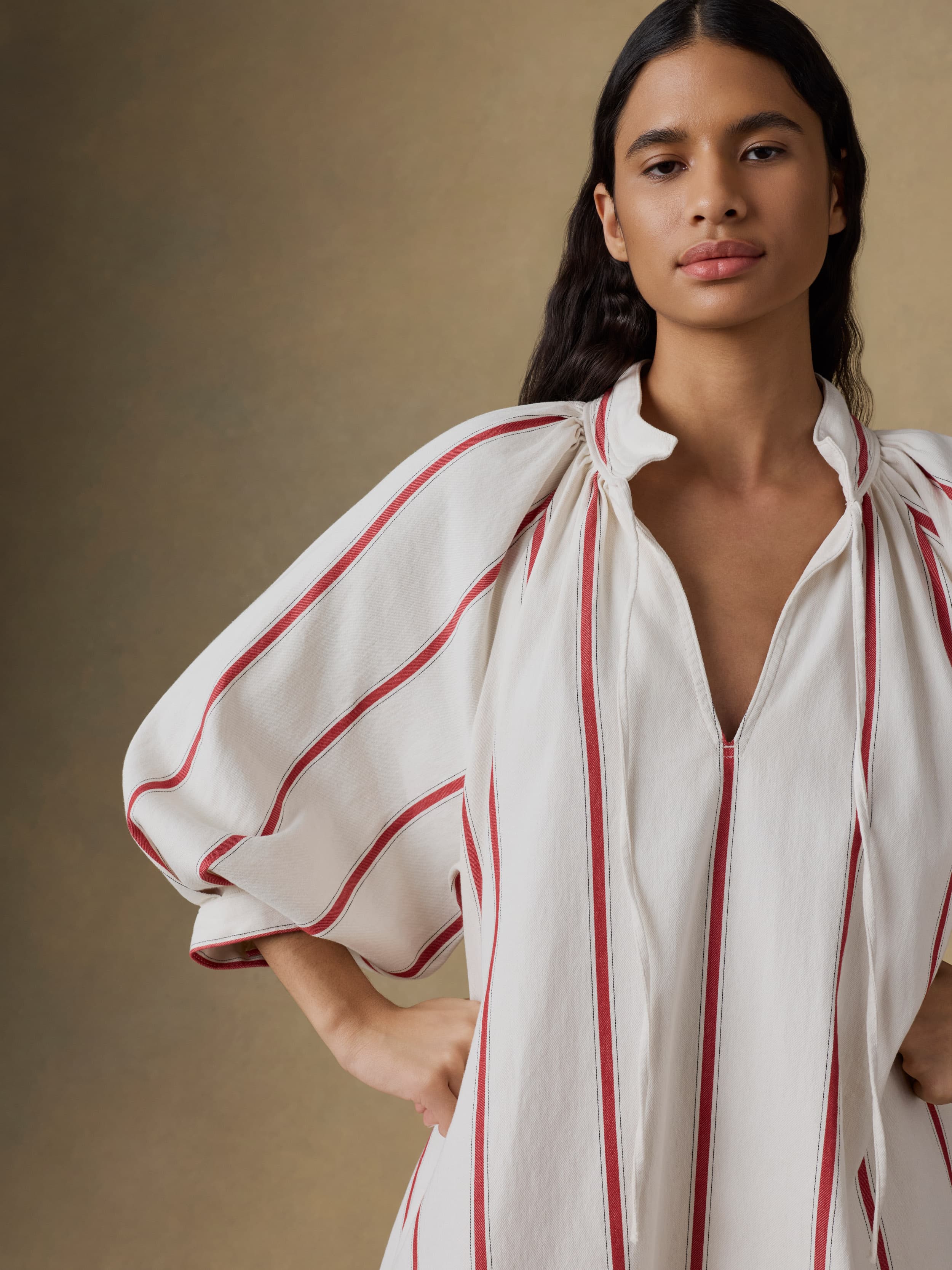 Woman wearing a white dress with red stripes against a beige background