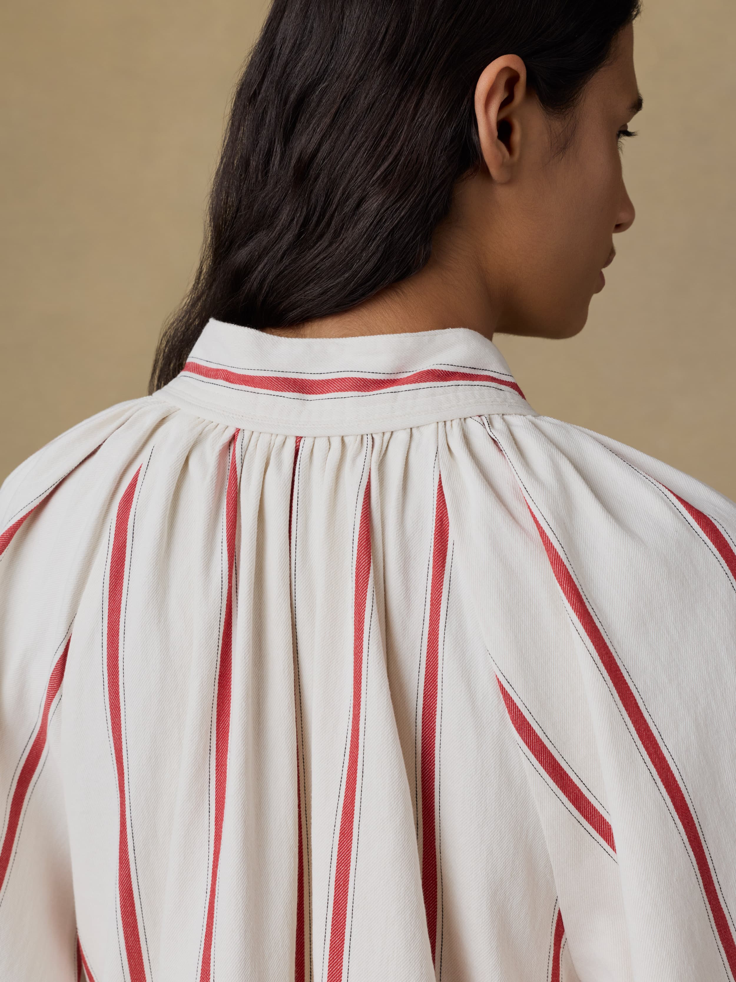 Close up of a woman wearing a white dress with red stripes against a beige background