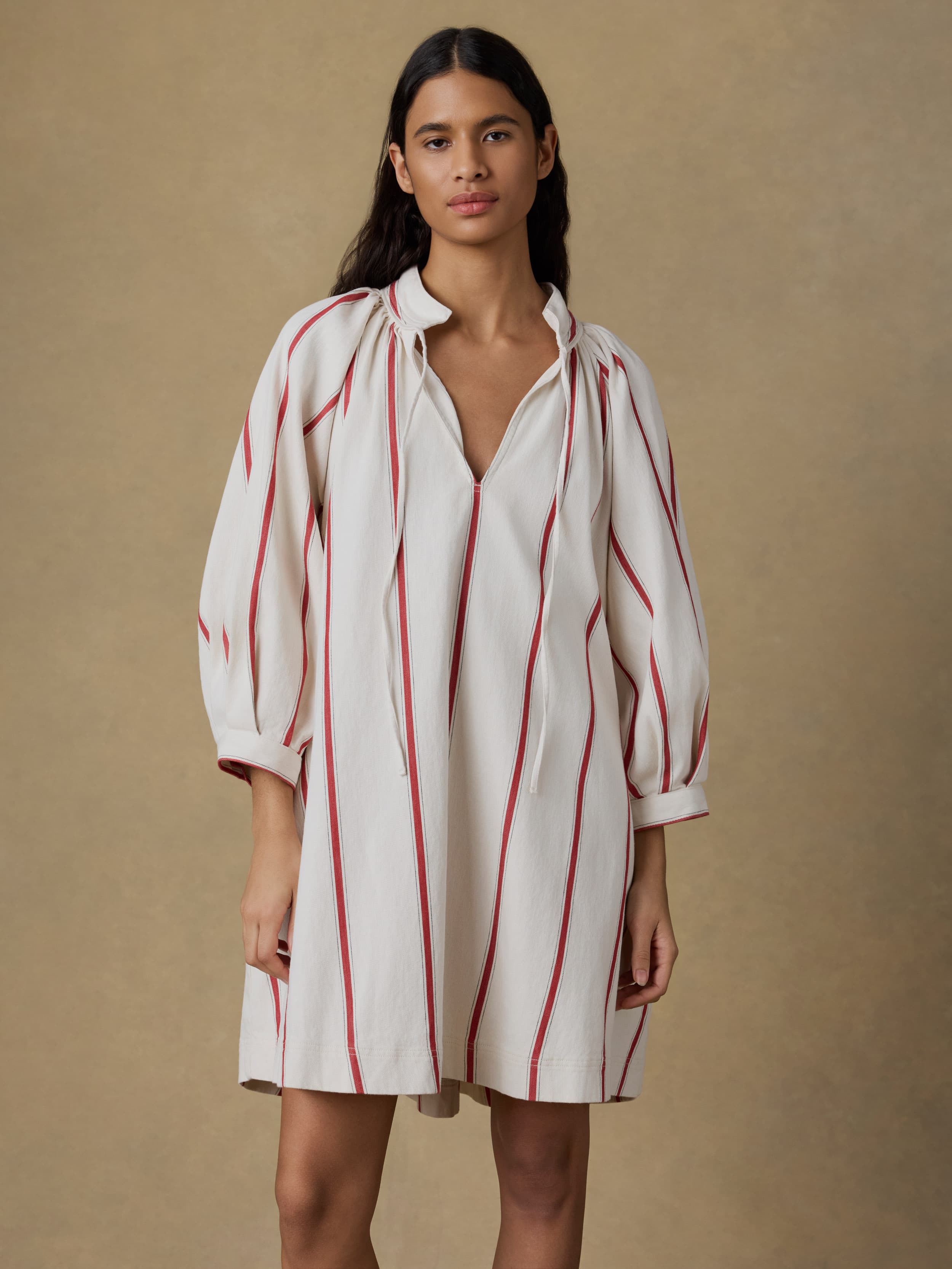 Woman wearing a white dress with red stripes against a beige background