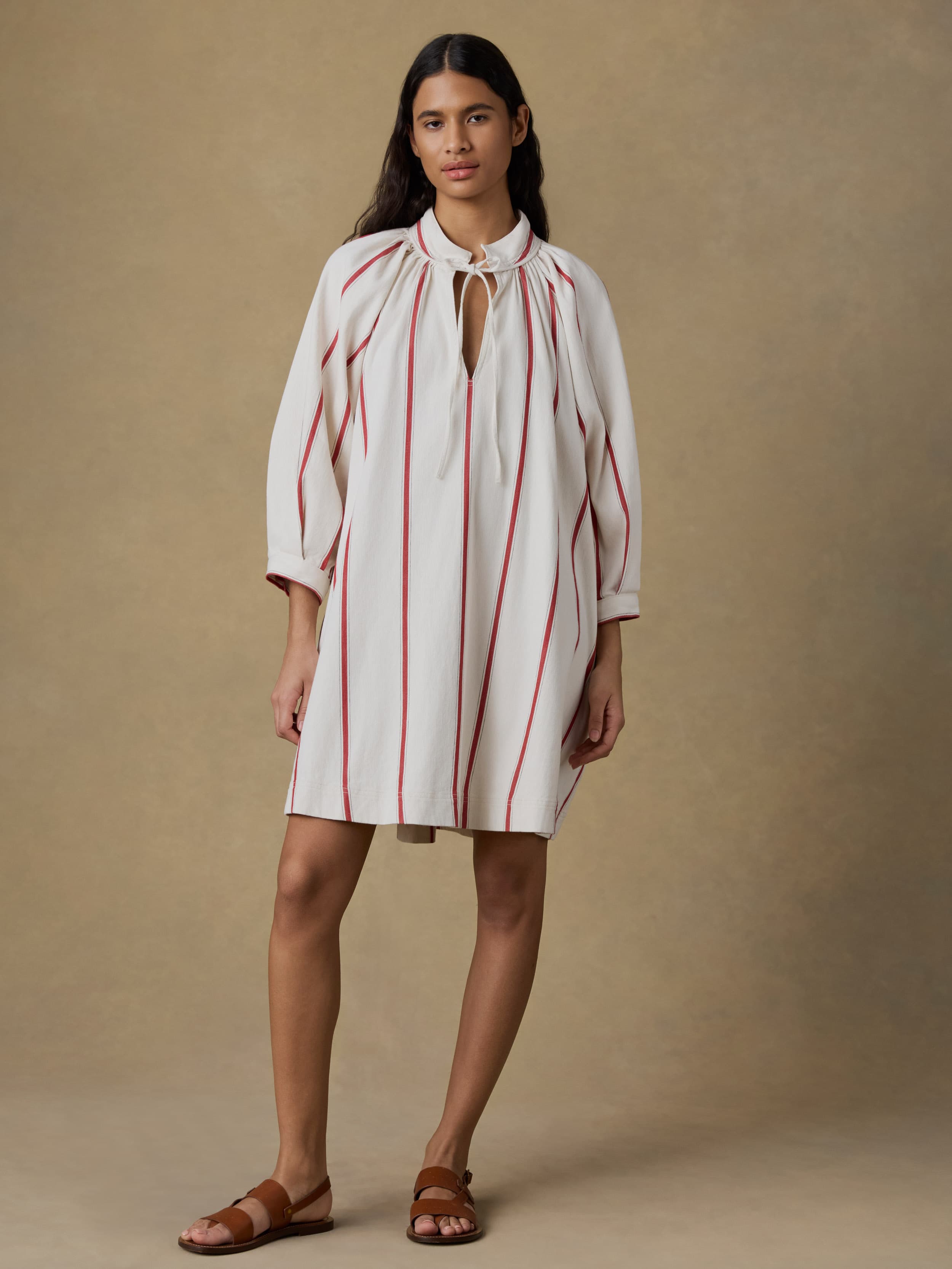 Woman wearing a white dress with red stripes against a beige background