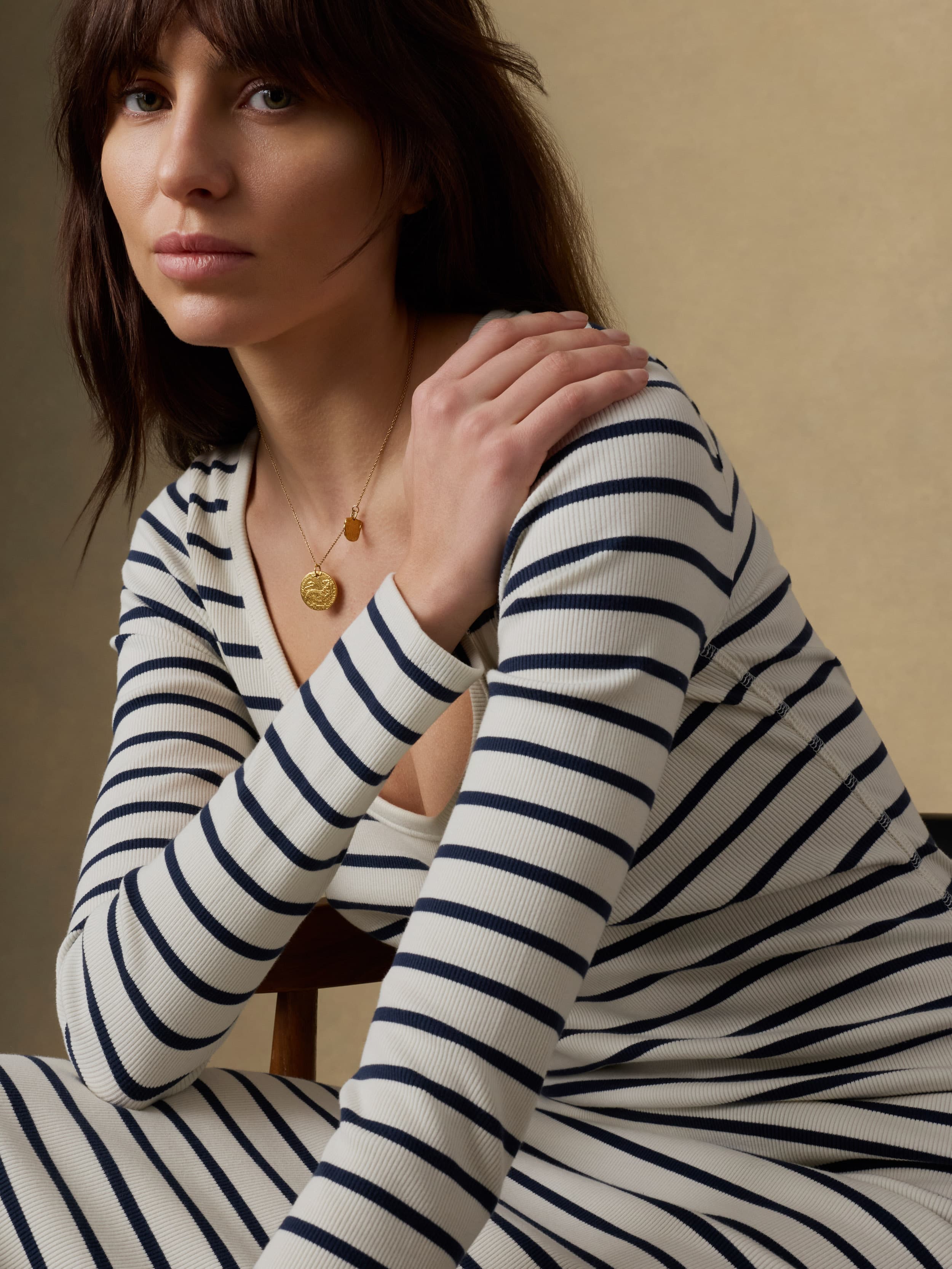 Close up of a woman wearing a long, navy and white striped dress against a beige background