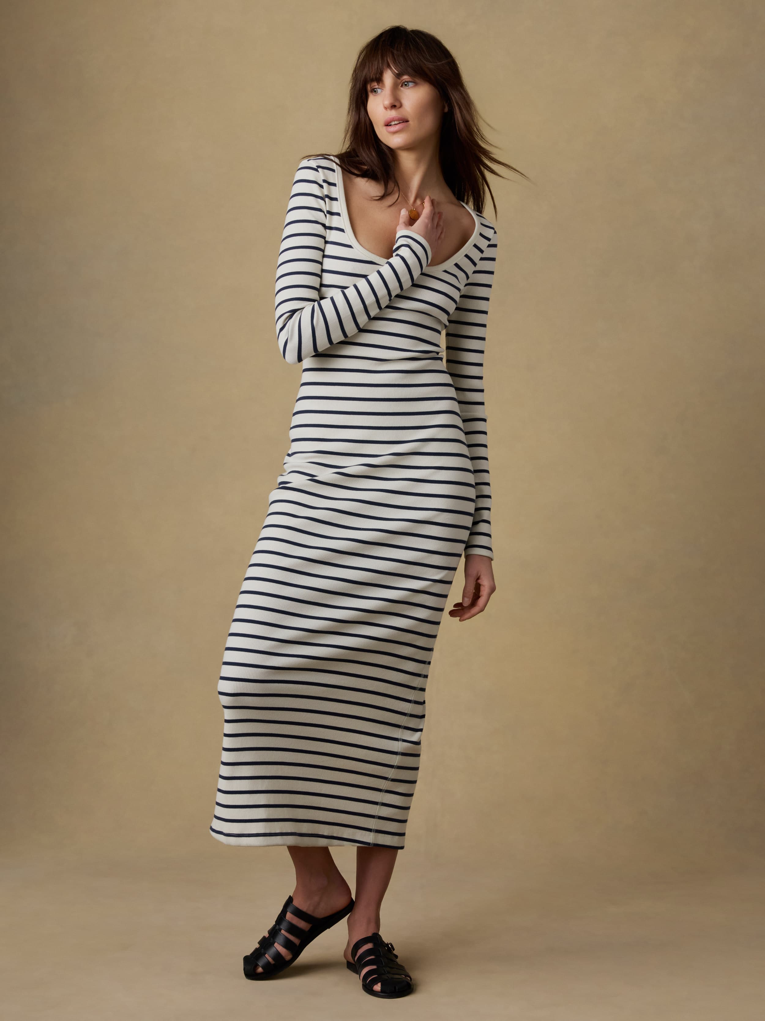 Woman wearing a long, navy and white striped dress against a beige background