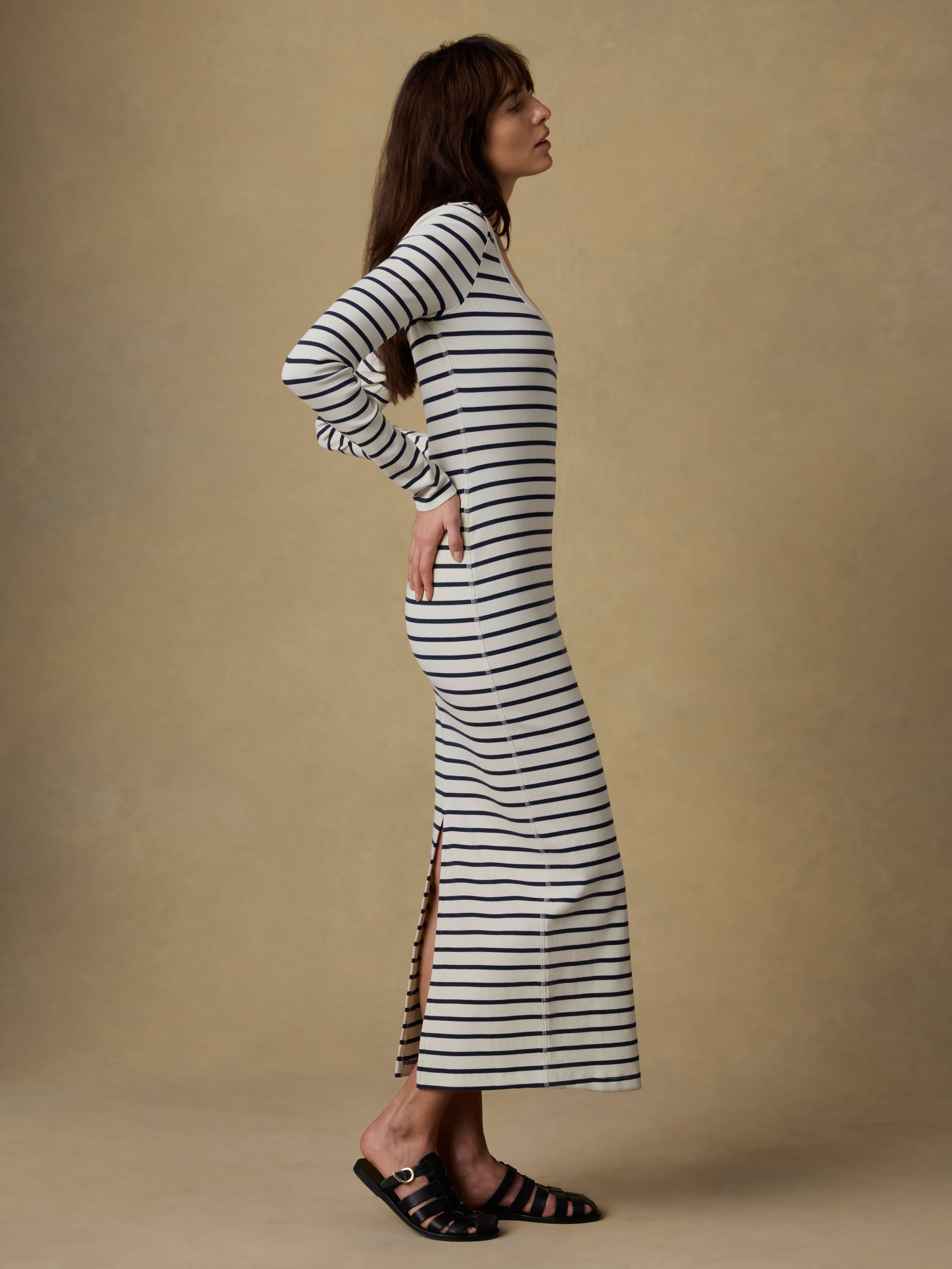Woman wearing a long, navy and white striped dress against a beige background
