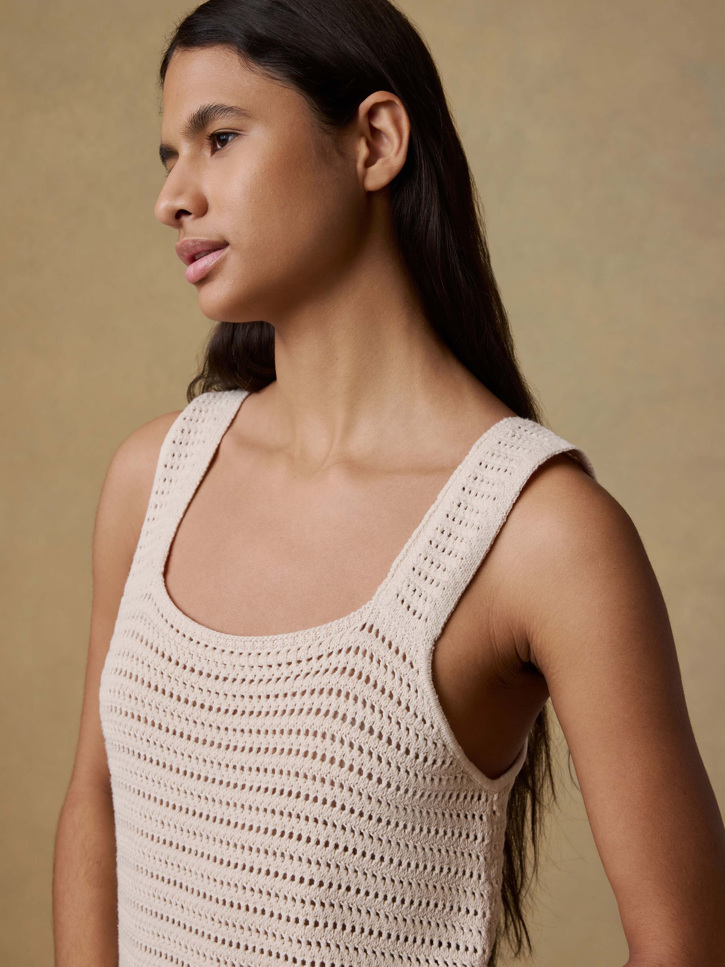 Woman wearing a cream crochet dress against a beige background
