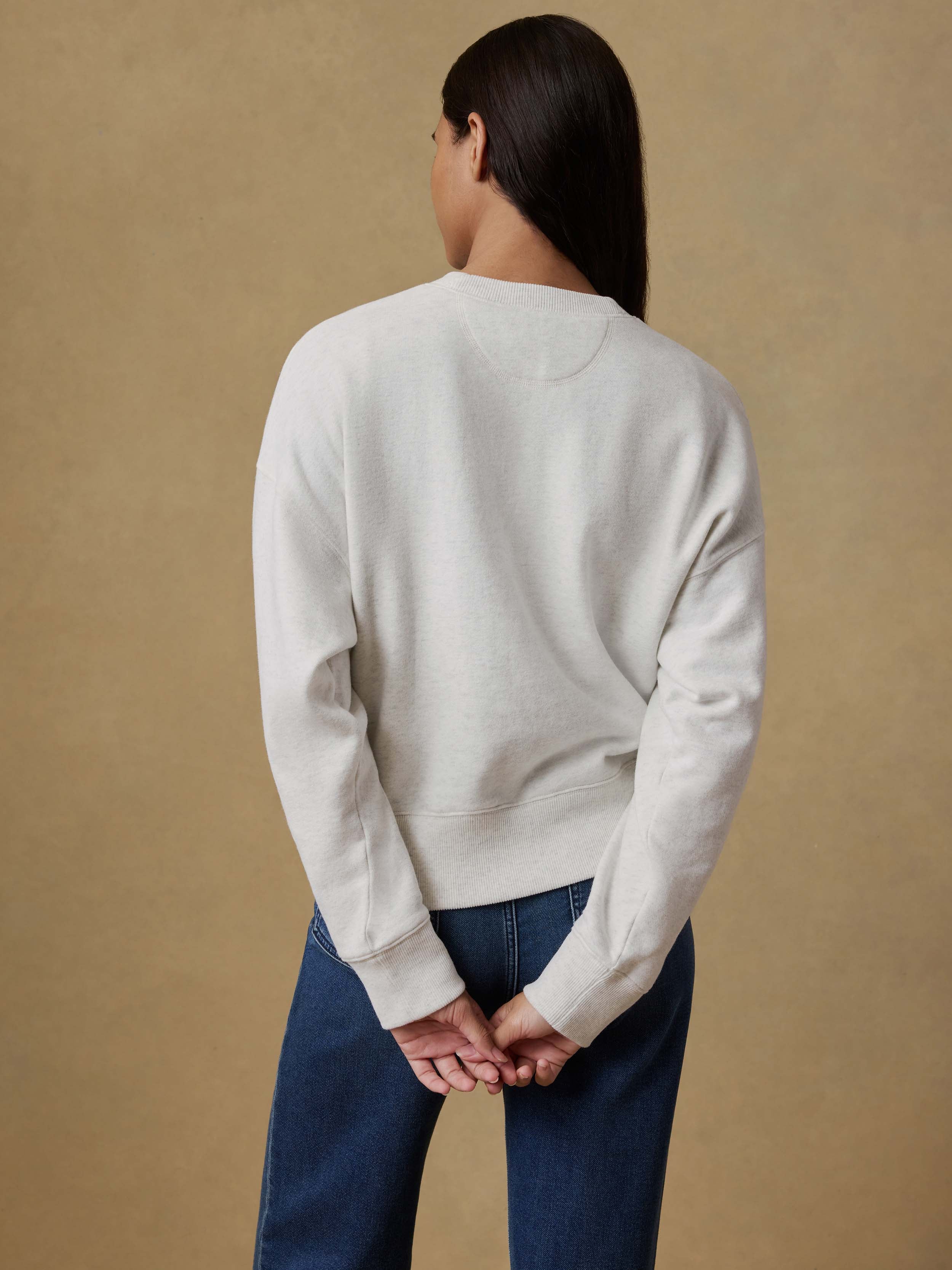 Woman wearing a light gray sweater and blue jeans against a beige background
