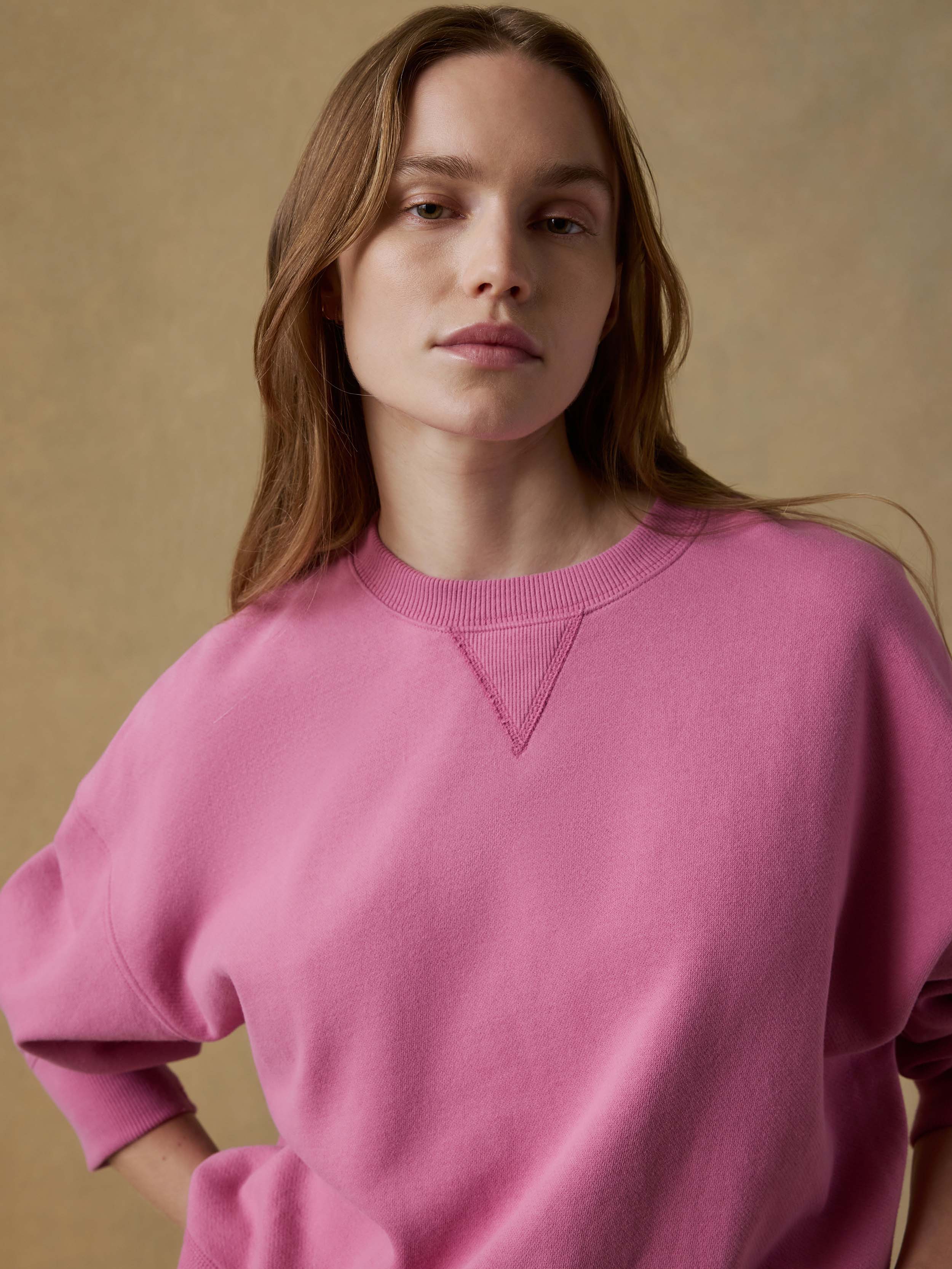 Woman wearing a pink sweatshirt against a beige background