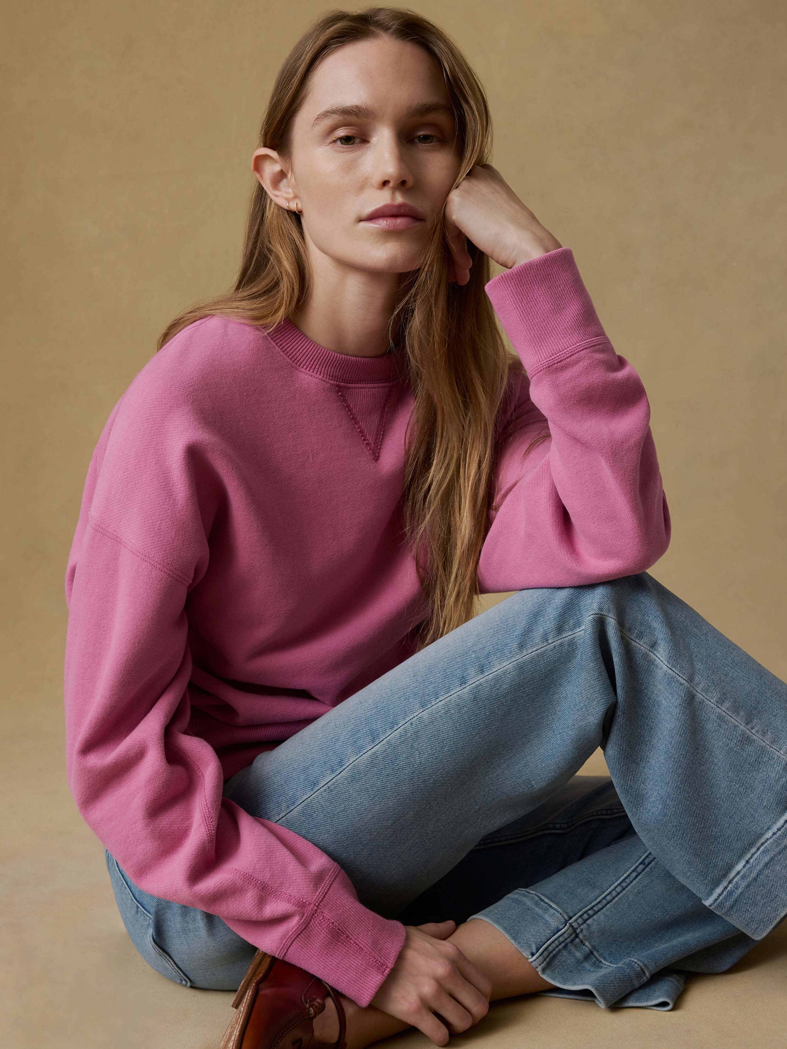 Woman wearing a pink sweatshirt and blue jeans against a beige background