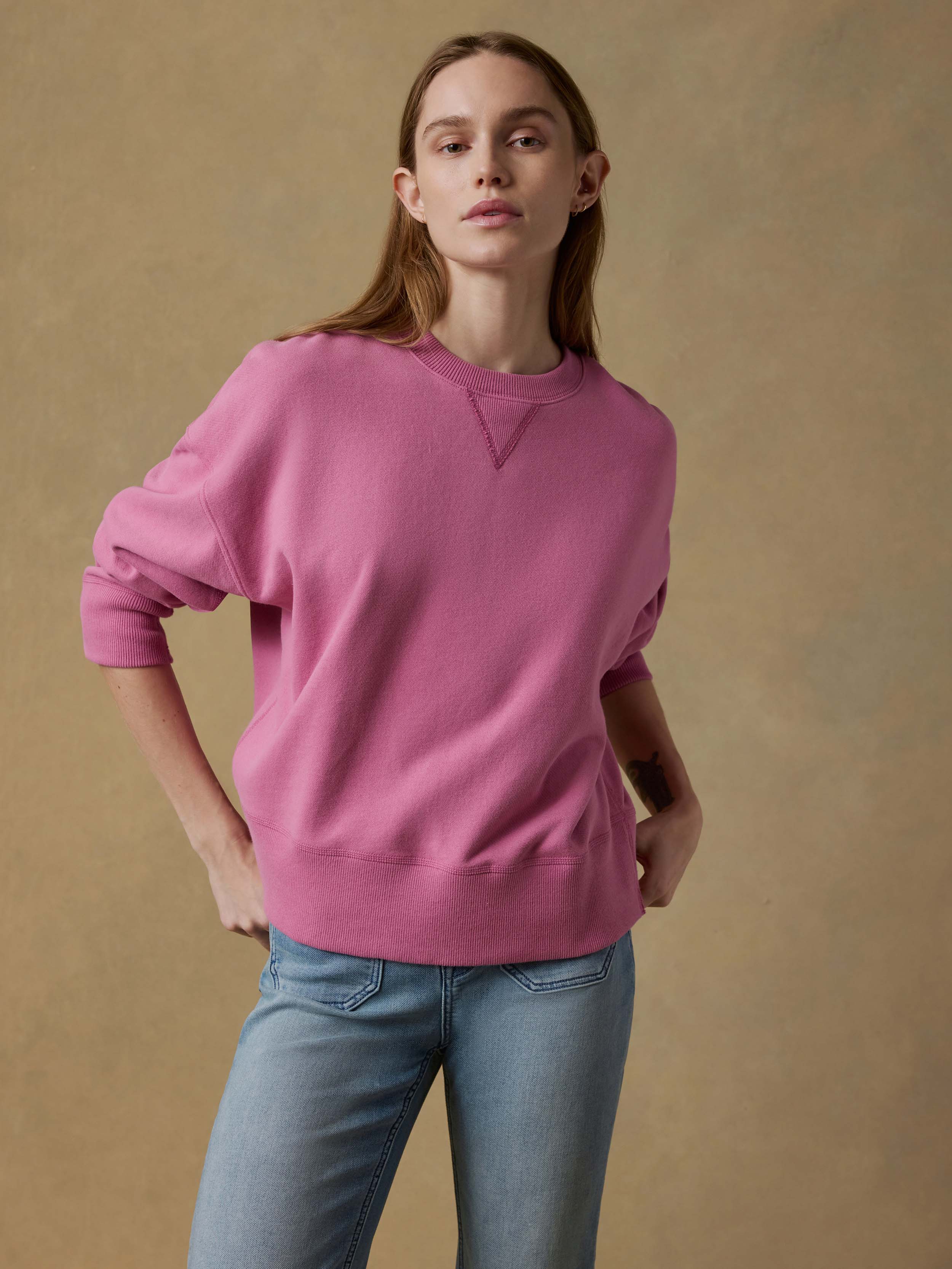 Woman wearing a pink sweatshirt and blue jeans against a beige background