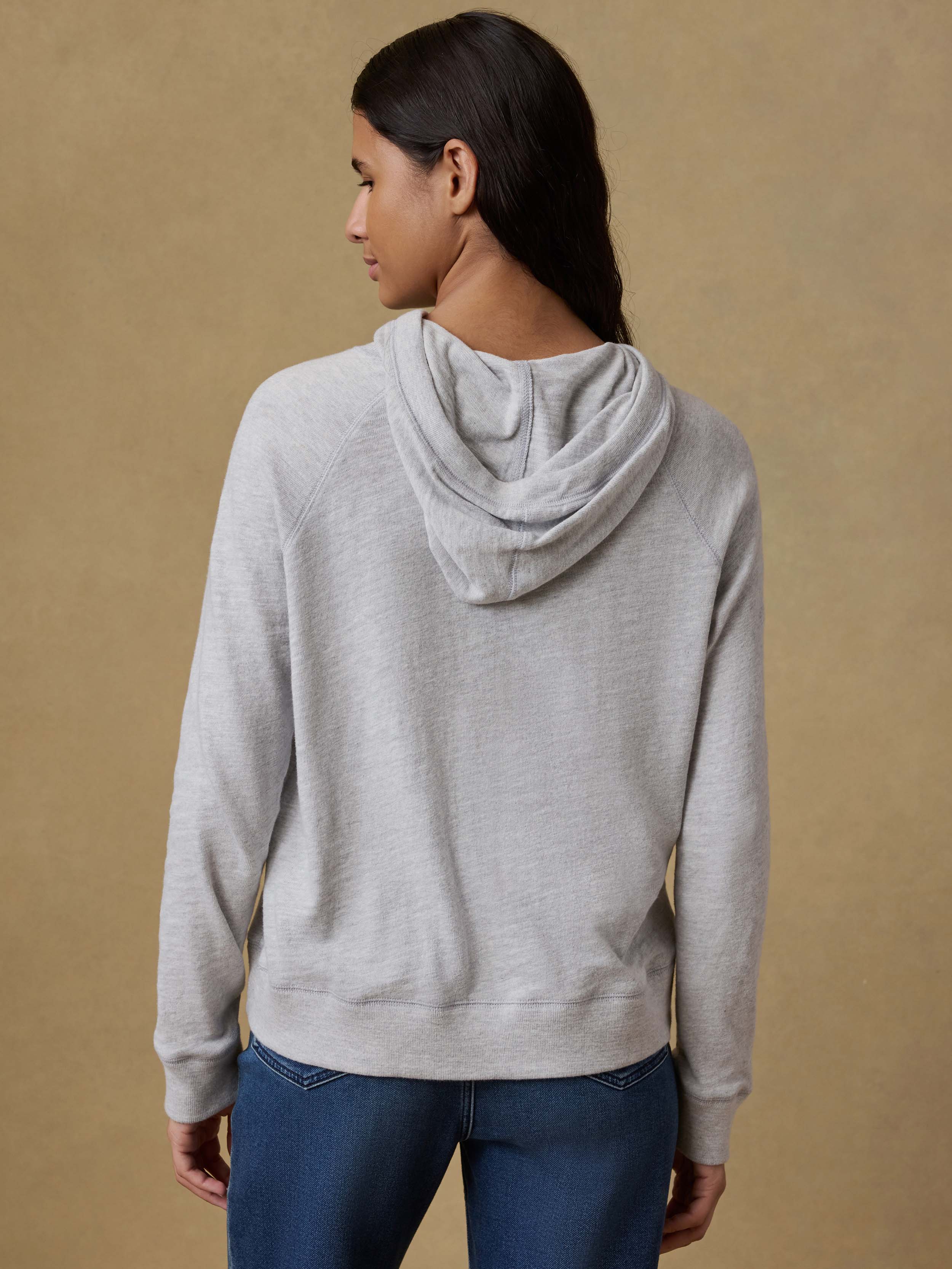Back view of a woman wearing a gray hoodie and blue stretch terry pants against a beige background