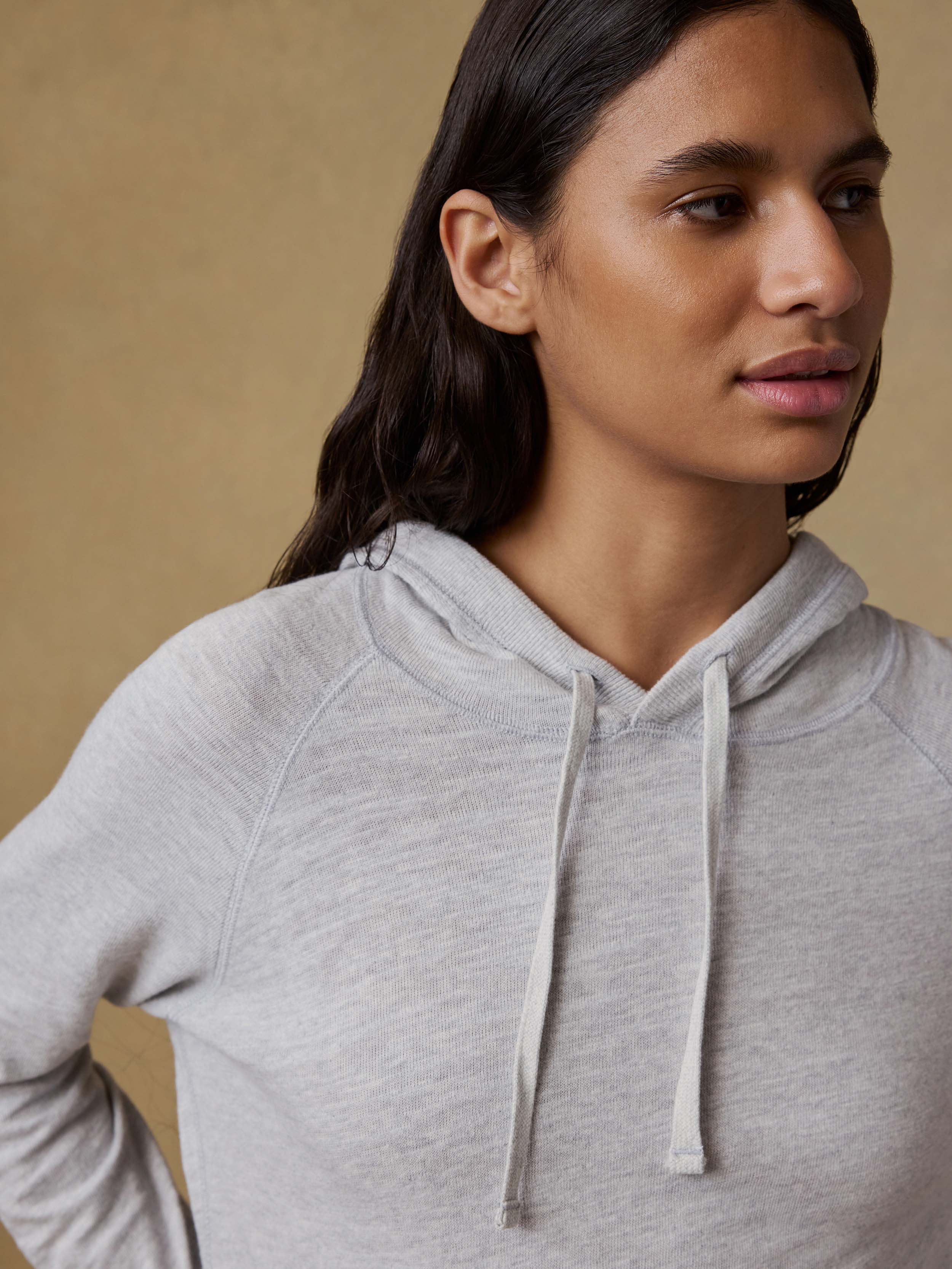 Woman wearing a gray hoodie against a beige background