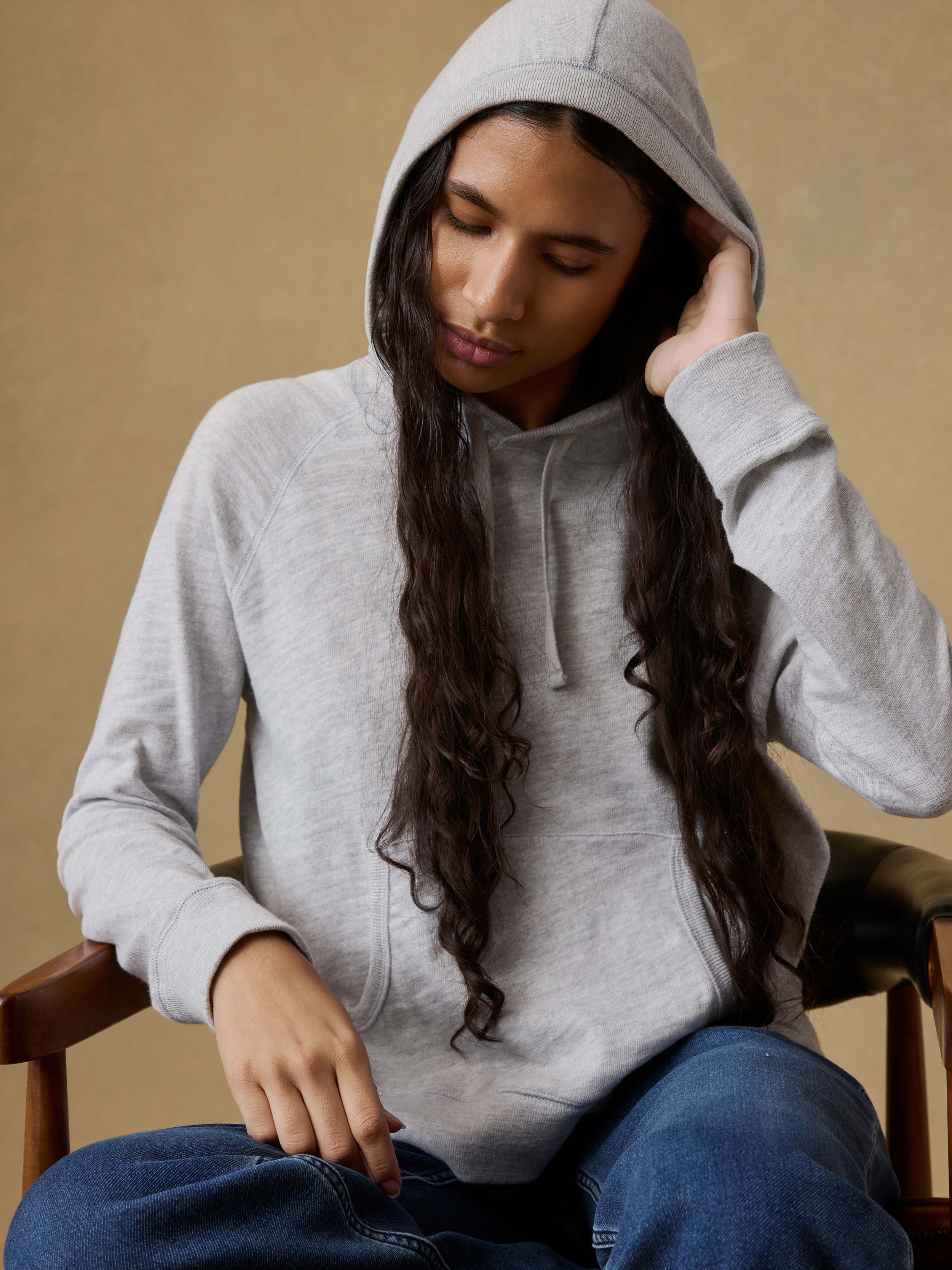 Woman sitting on a chair wearing a gray hoodie and blue stretch terry pants against a beige background