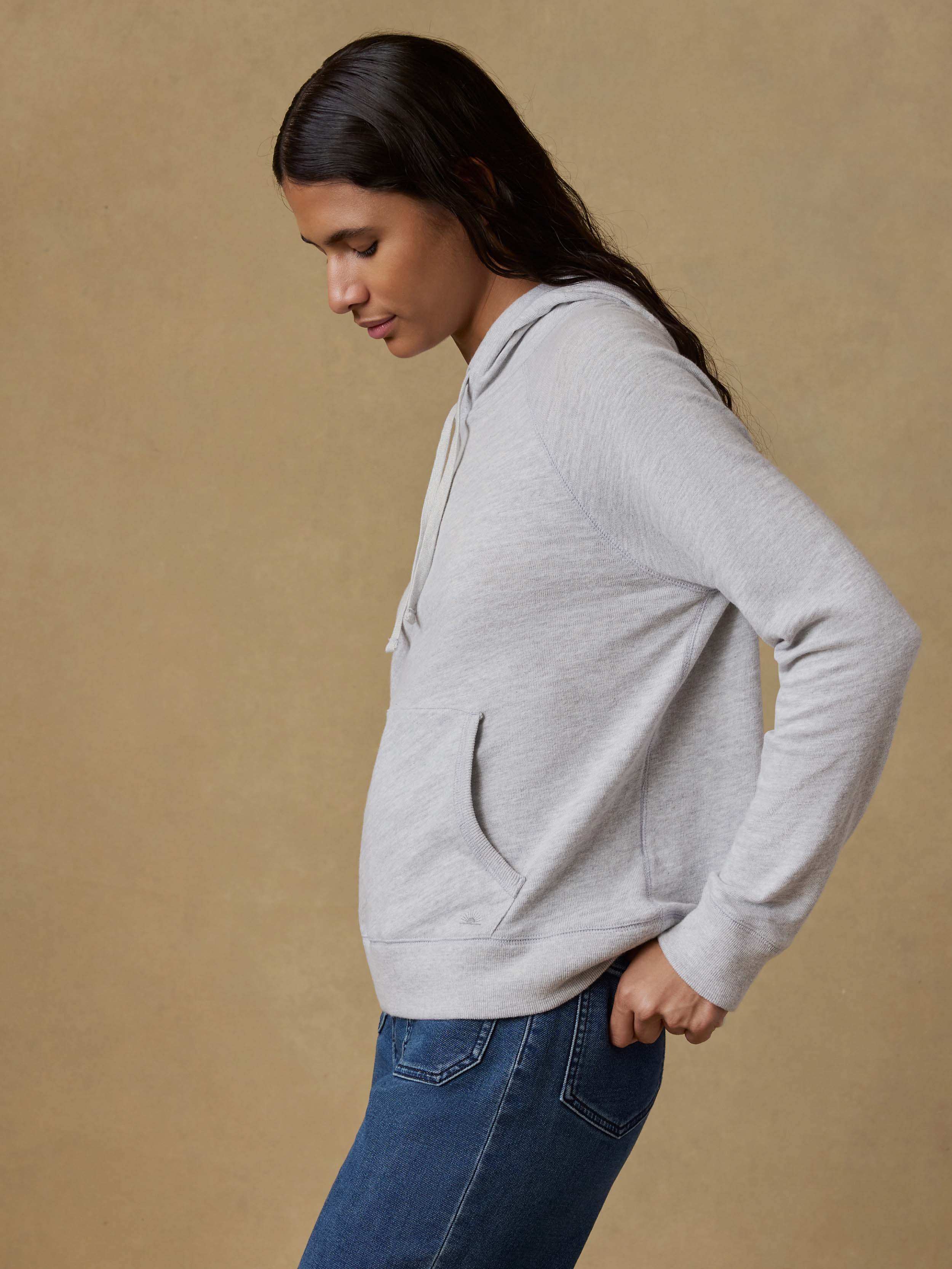 Woman wearing a gray hoodie and blue stretch terry pants against a beige background