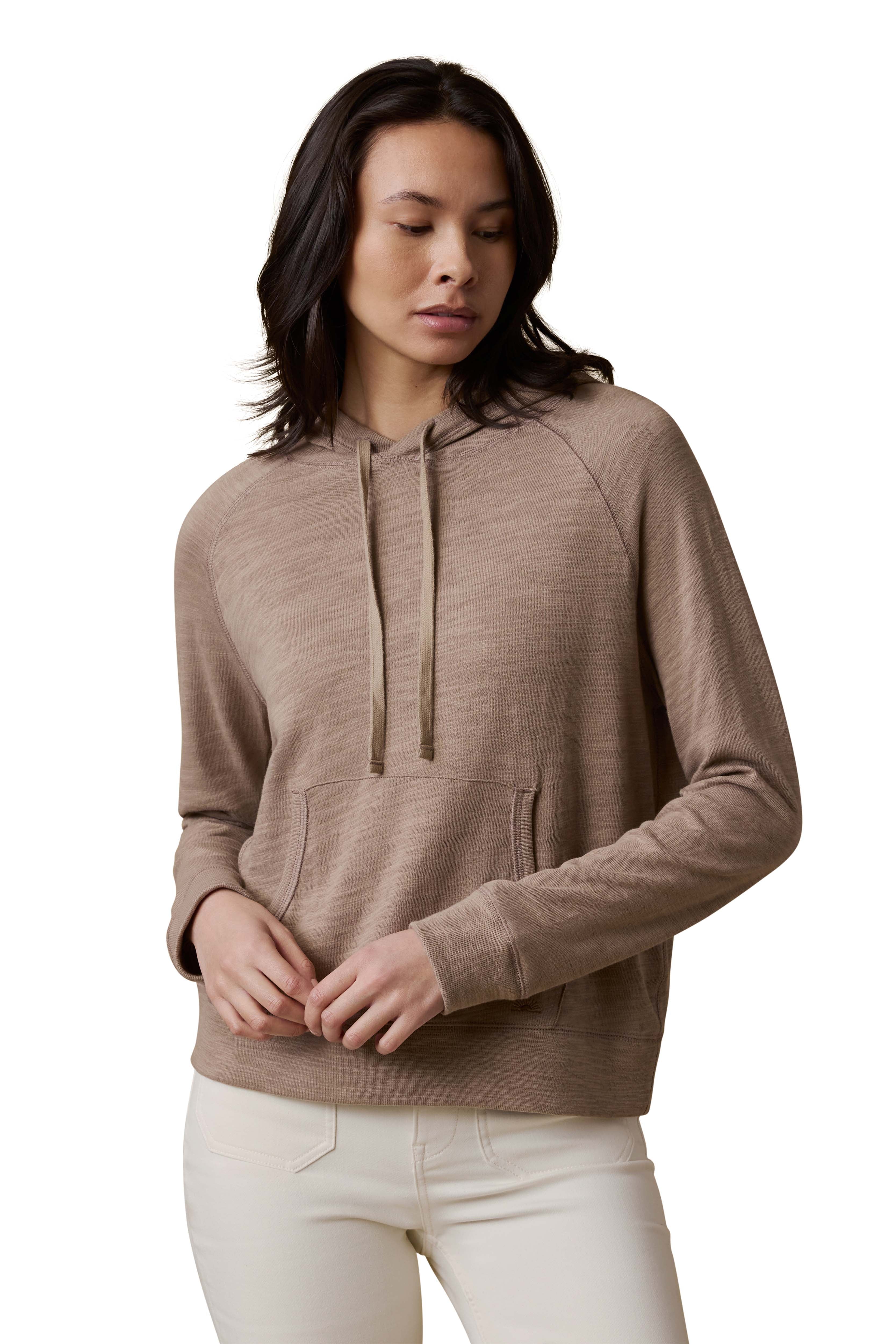 A woman wearing a beige hoodie and white pants