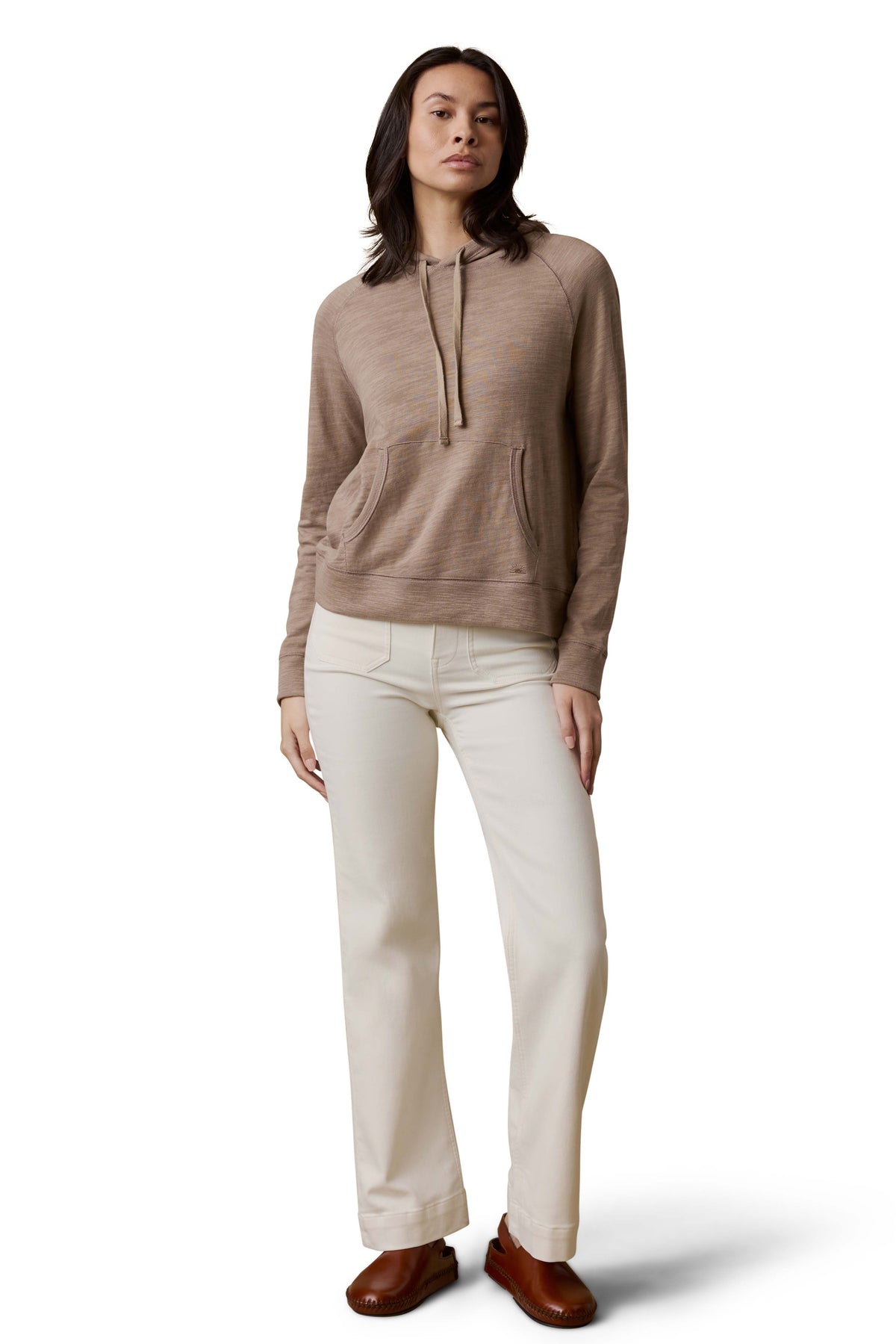 A woman wearing a beige hoodie, white pants, and brown shoes, image 2 of 3