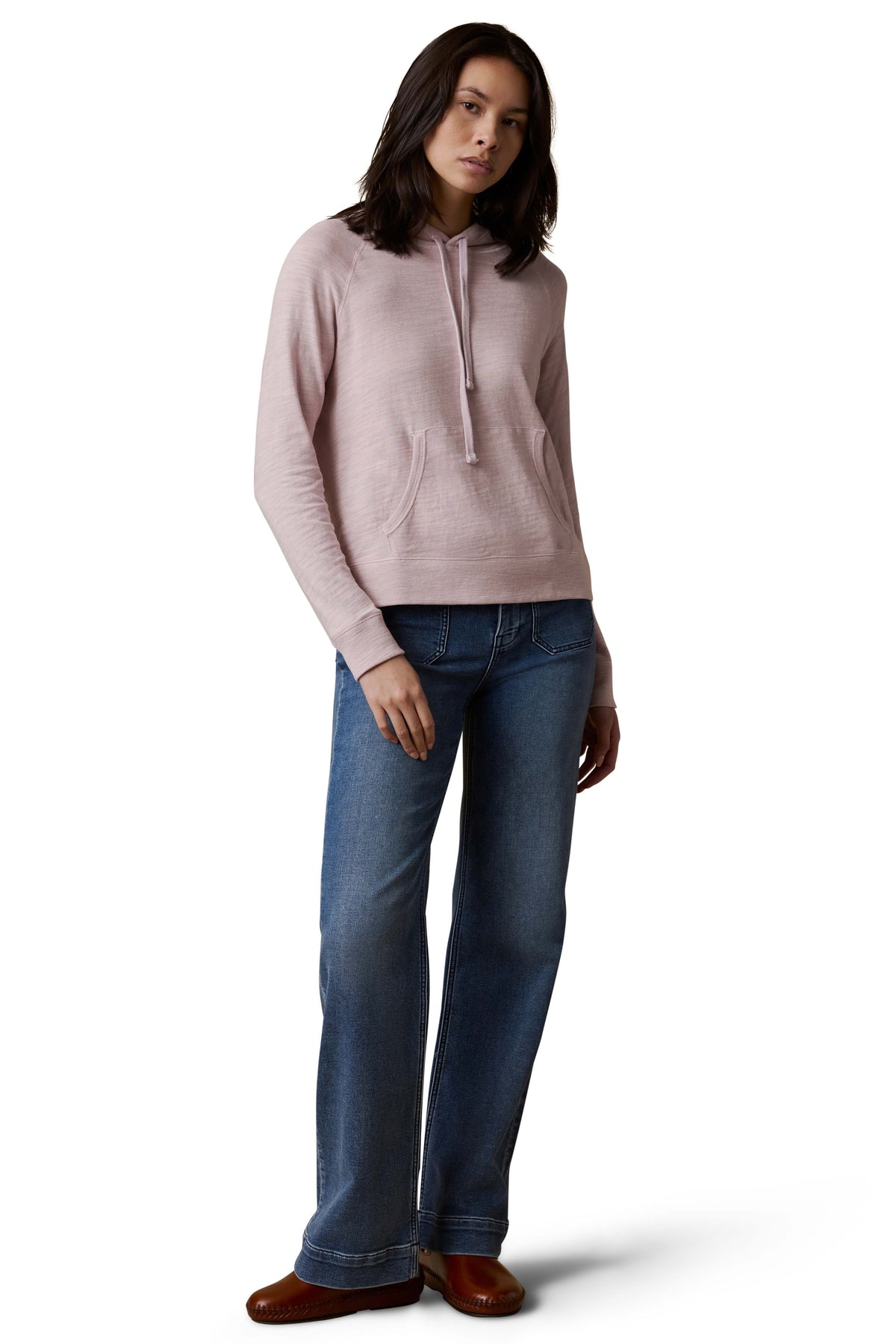 A woman wearing a light purple hoodie, blue jeans, and brown shoes, image 2 of 3