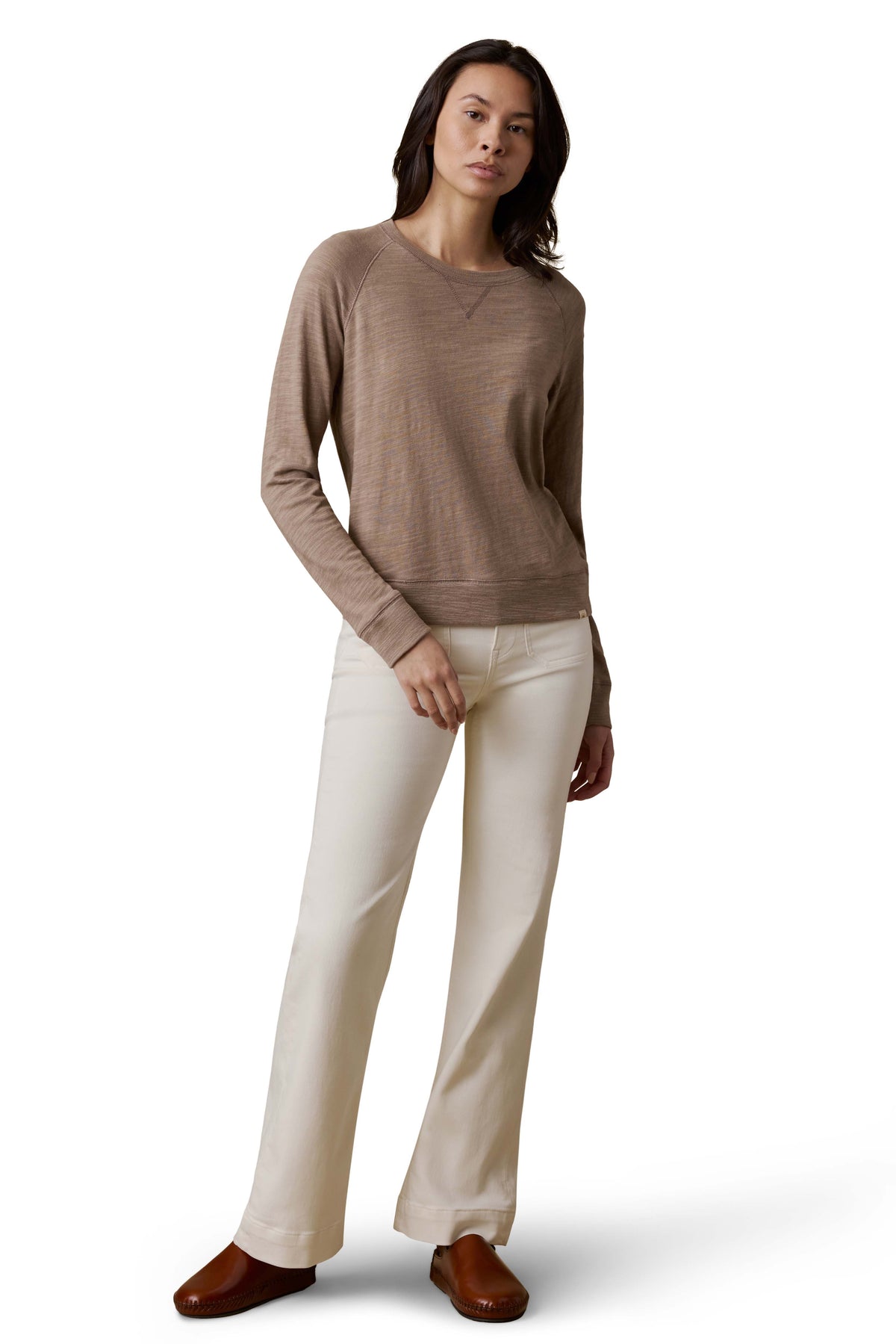 A woman wearing a beige crewneck, white pants, and brown shoes, image 2 of 3
