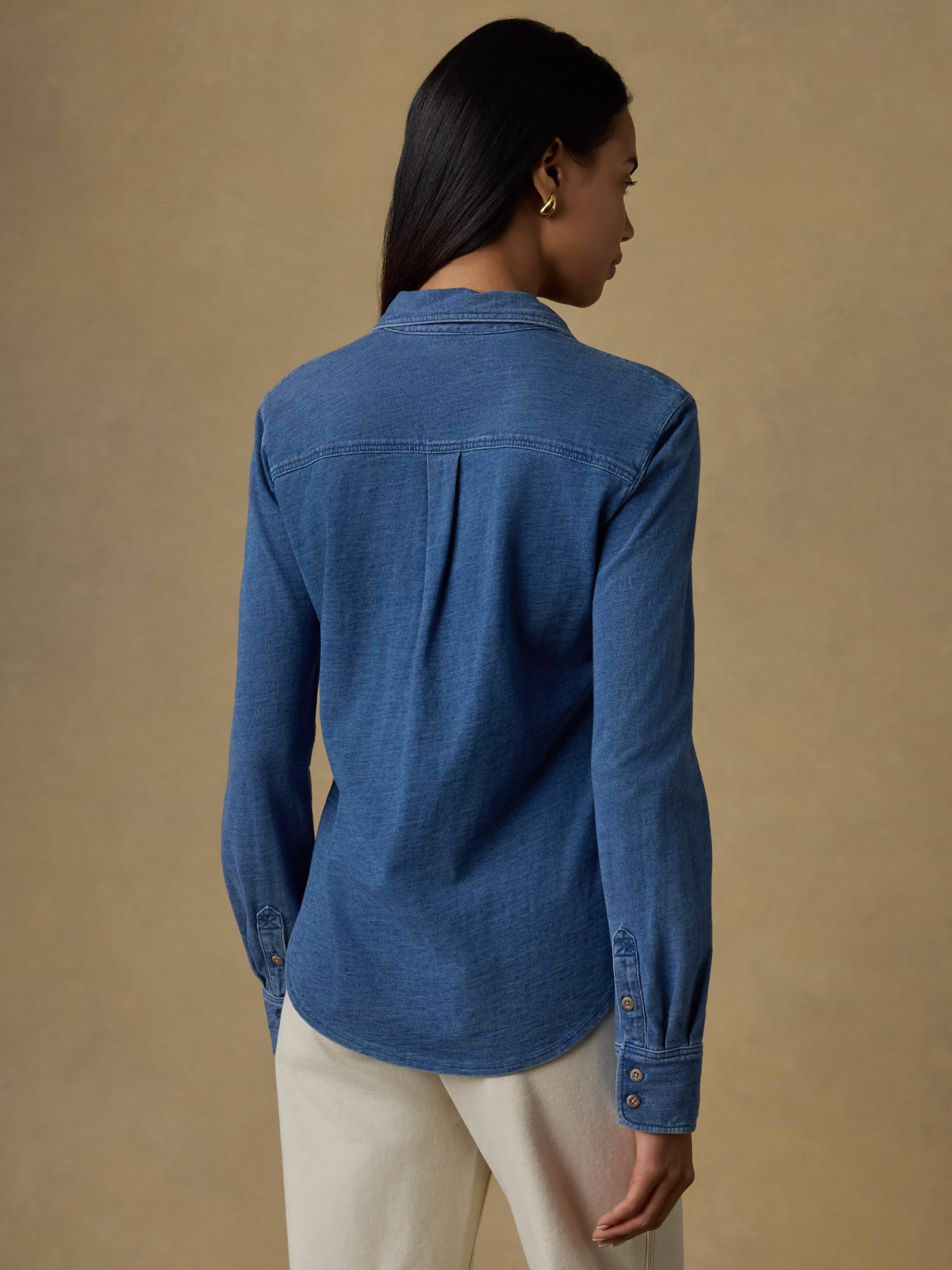 Back view of a woman wearing a blue denim shirt against a beige background
