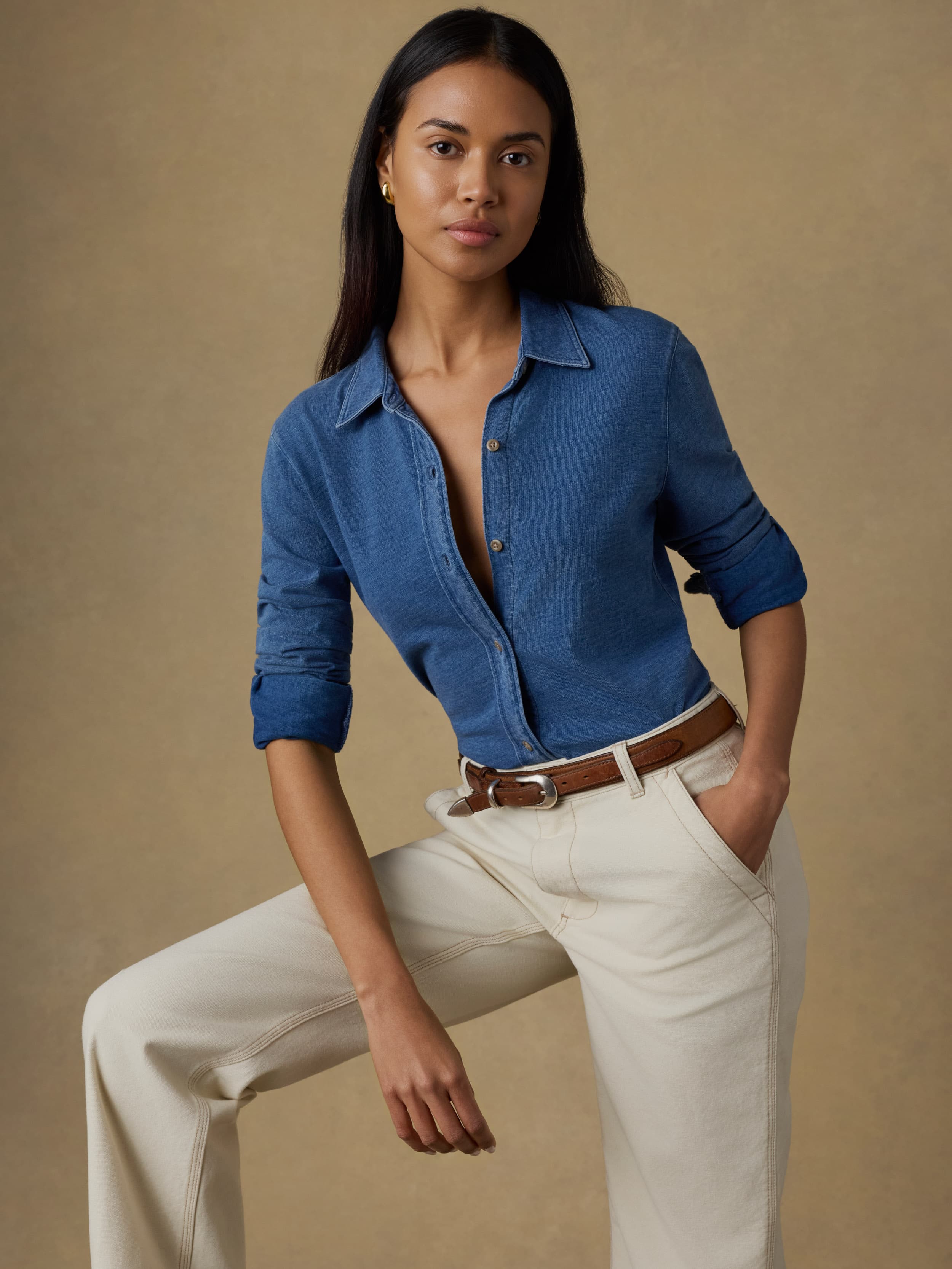 Woman wearing a blue shirt and beige pants against a brown background
