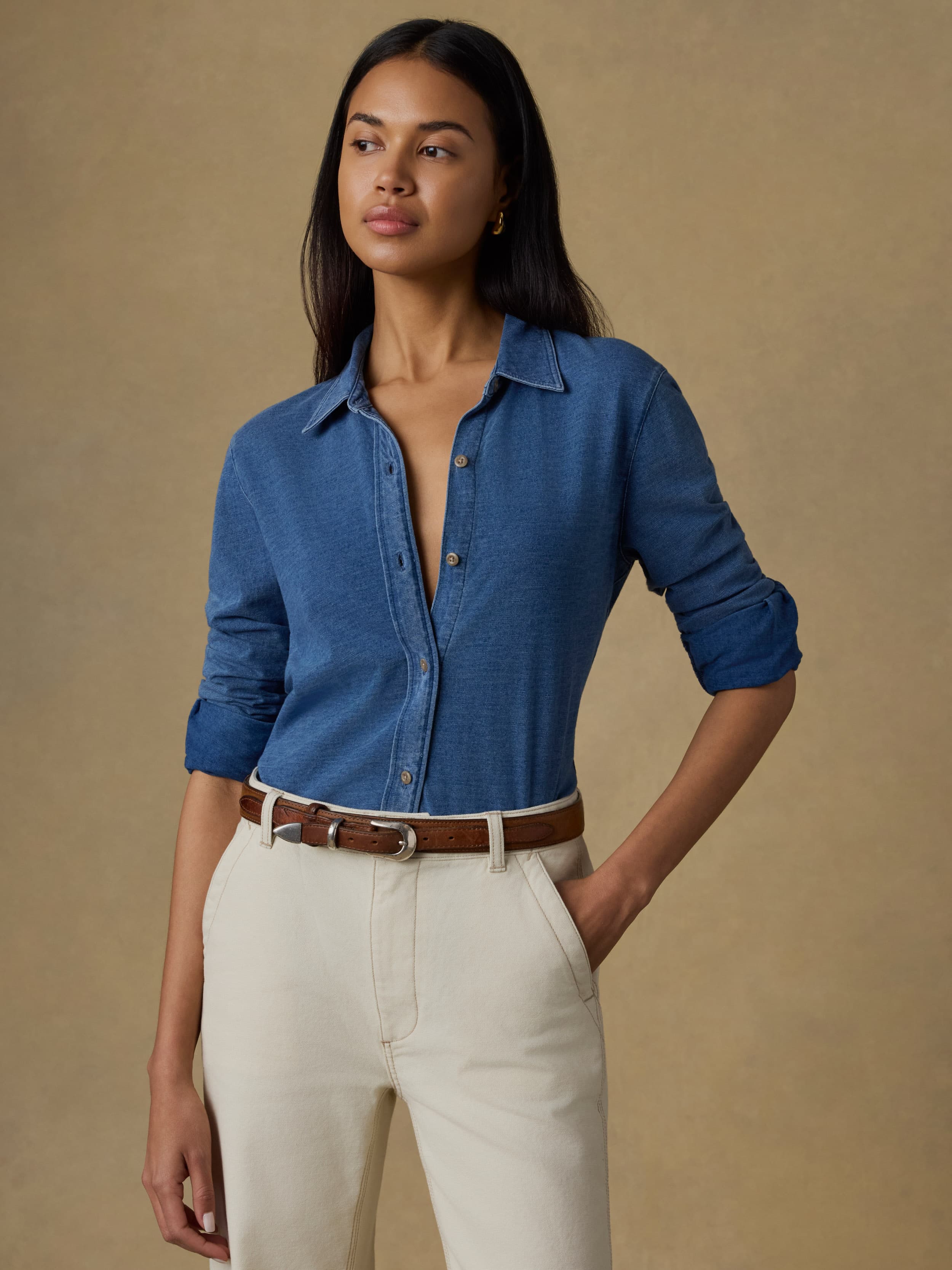 Woman wearing a blue shirt and white pants against a beige background