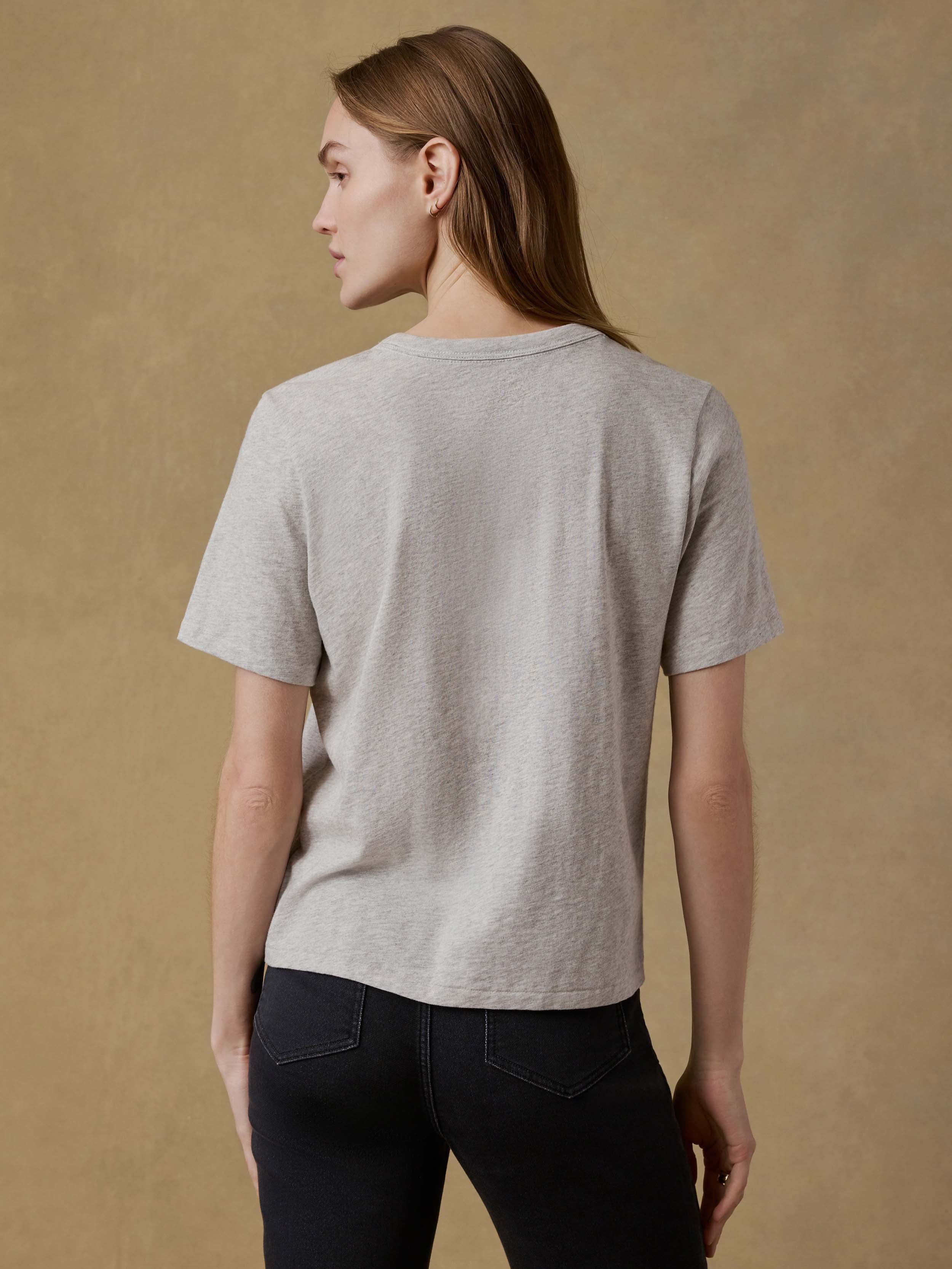 Back view of a woman wearing a gray t-shirt and black pants against a beige background