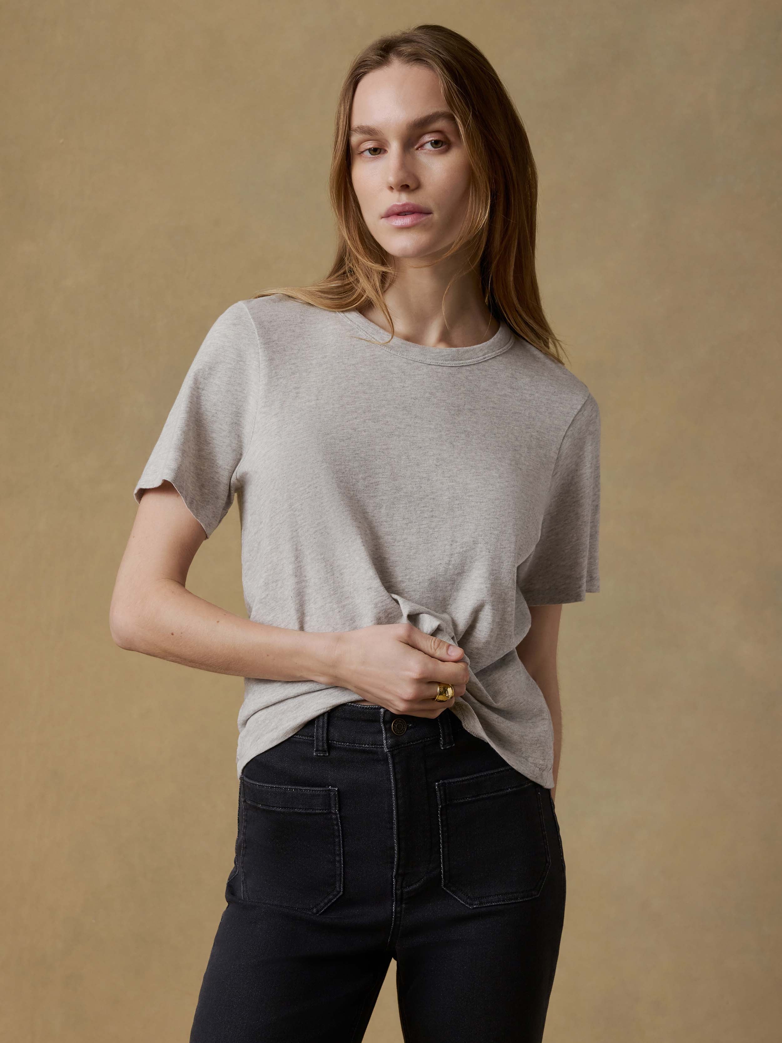 Woman wearing a gray t-shirt and black pants against a beige background