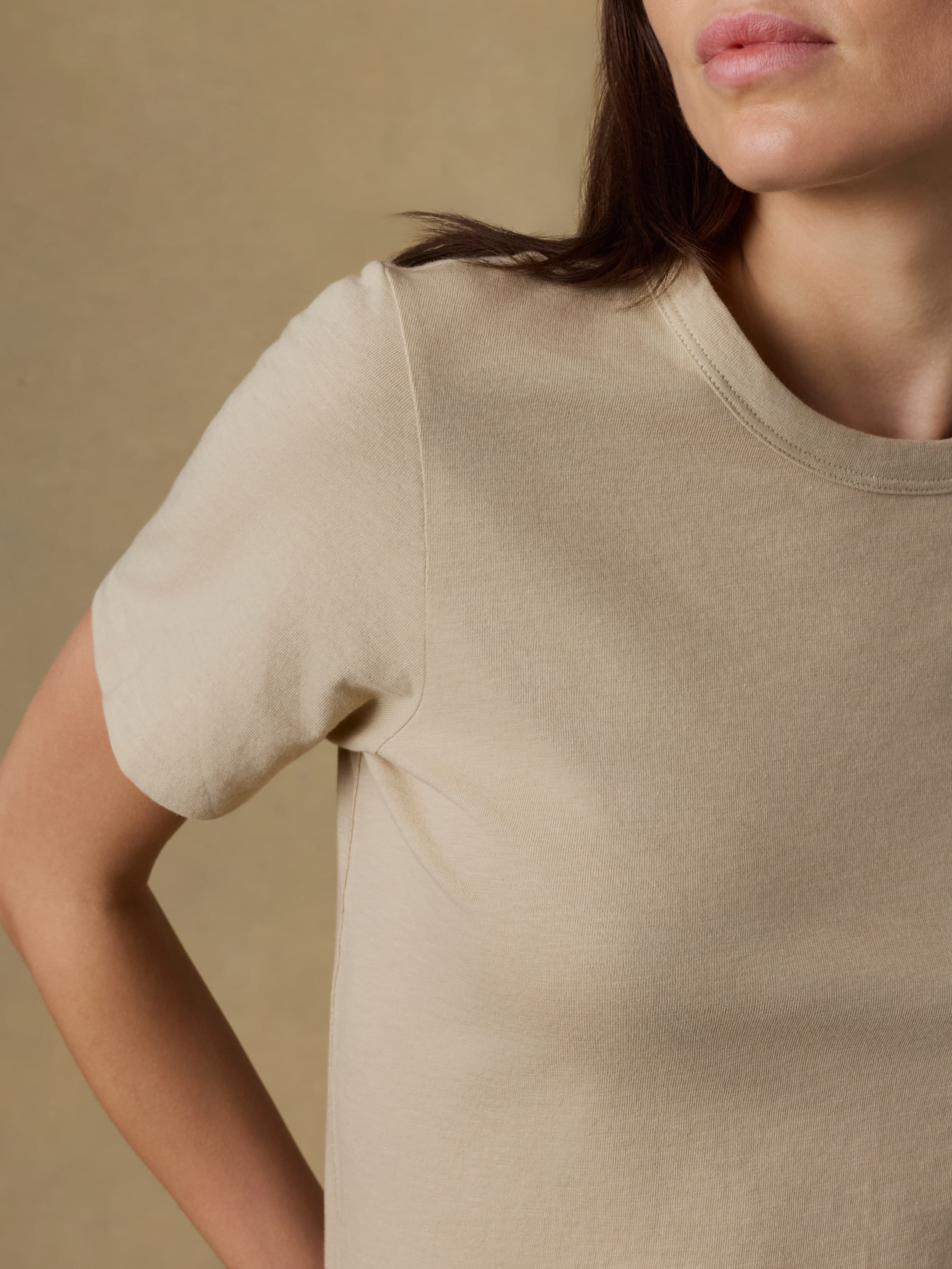 Close up of a woman wearing a beige t-shirt against a beige background