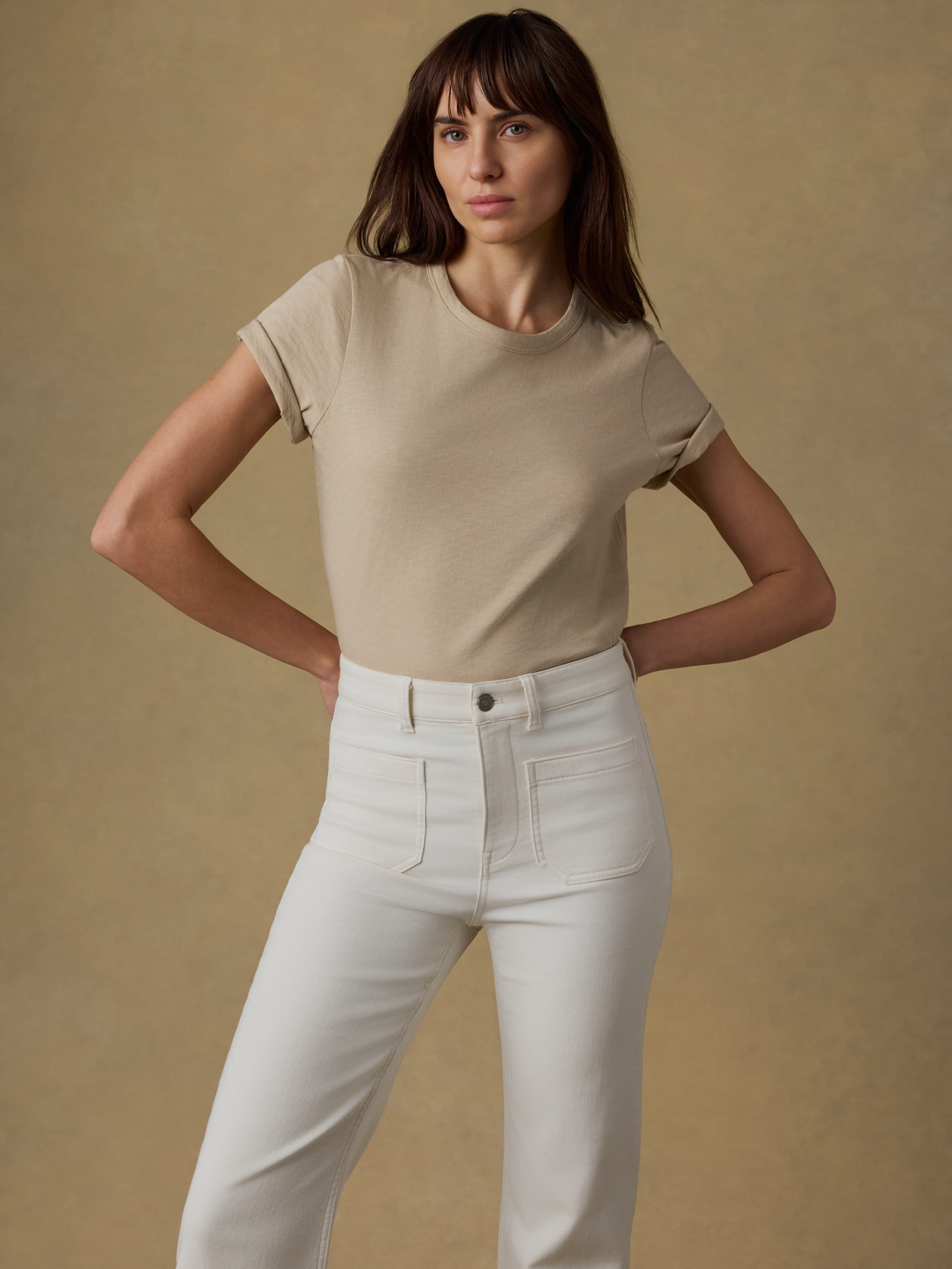 Woman wearing a beige t-shirt and white jeans against a beige background