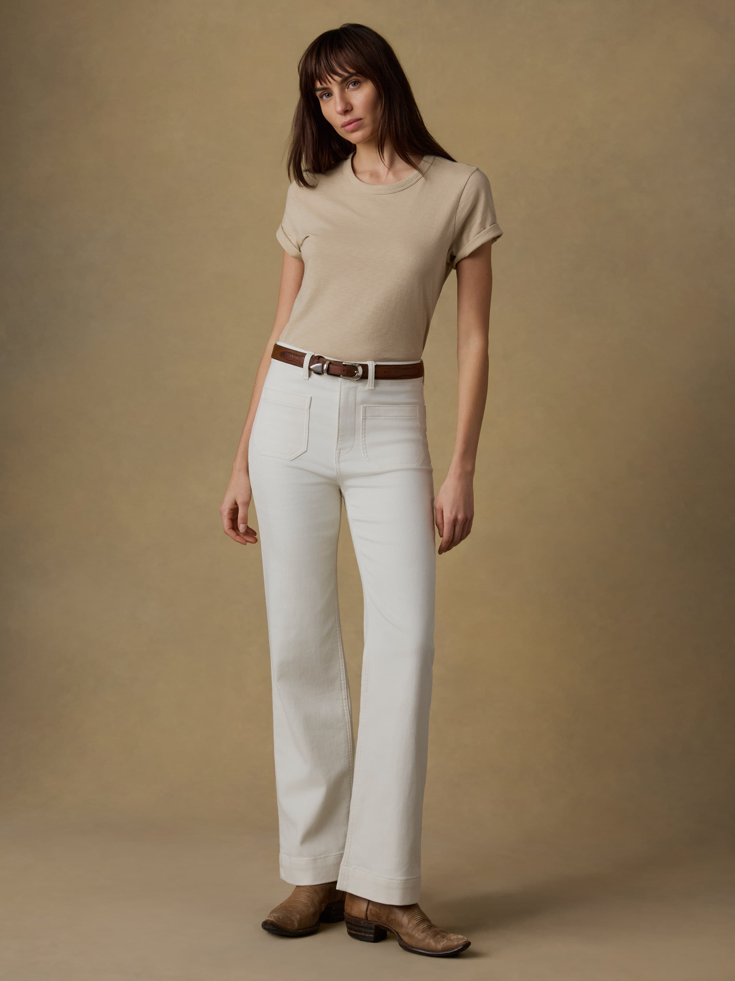 Woman wearing a beige t-shirt and white jeans against a beige background