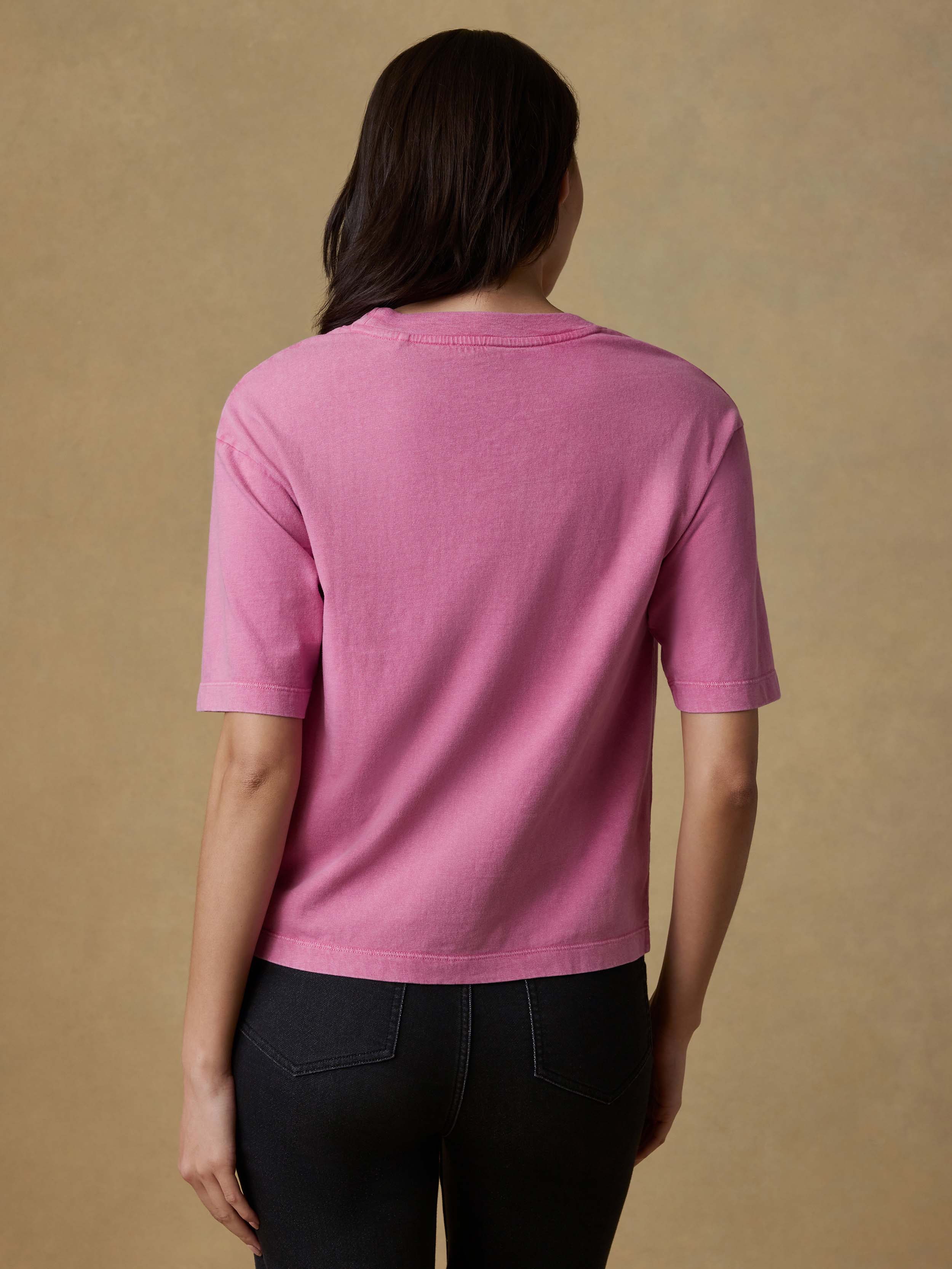 Back view of a woman wearing a pink t-shirt and black stretch terry pants against a beige background