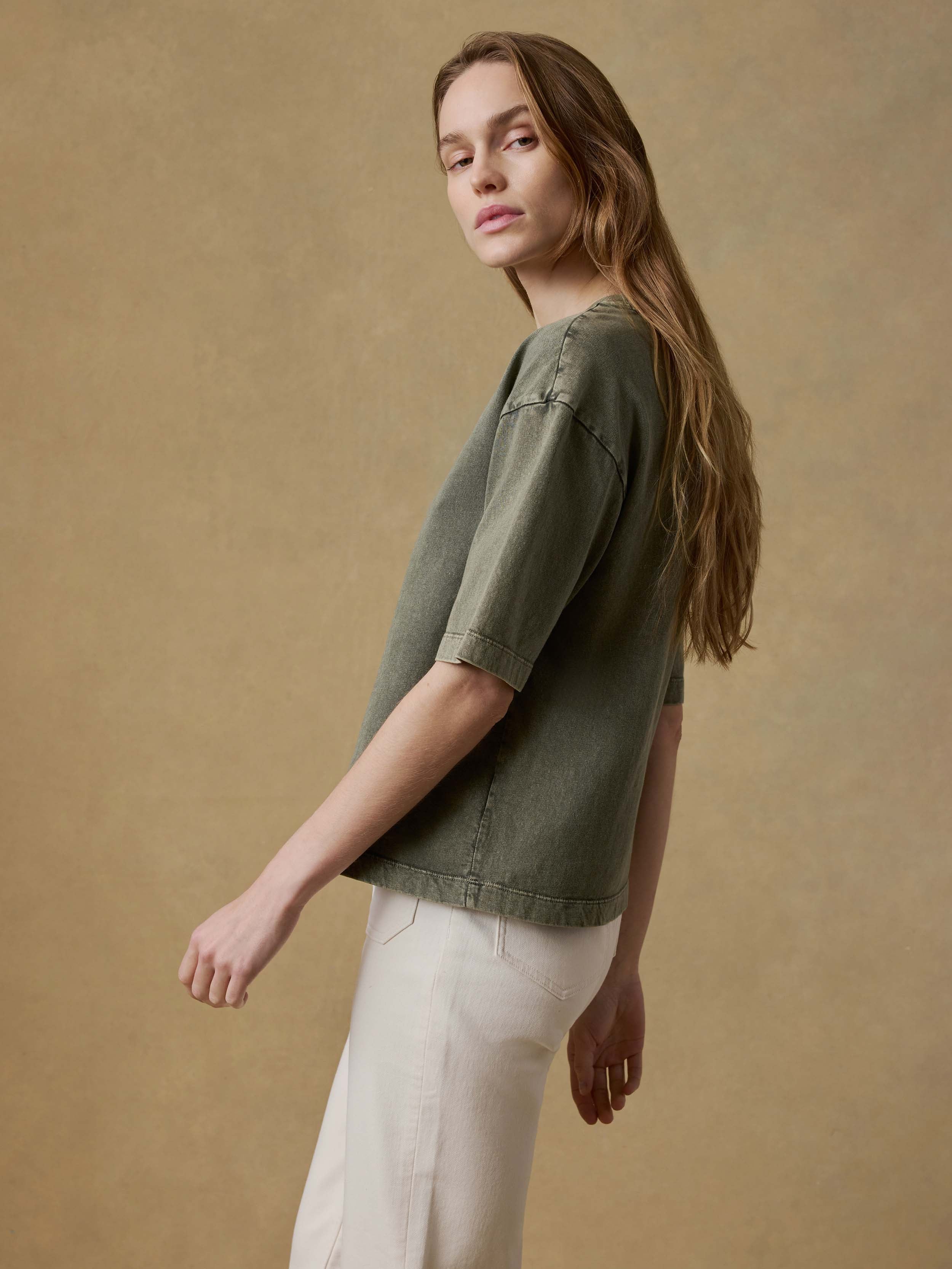 Woman wearing a green t-shirt and white pants against a beige background