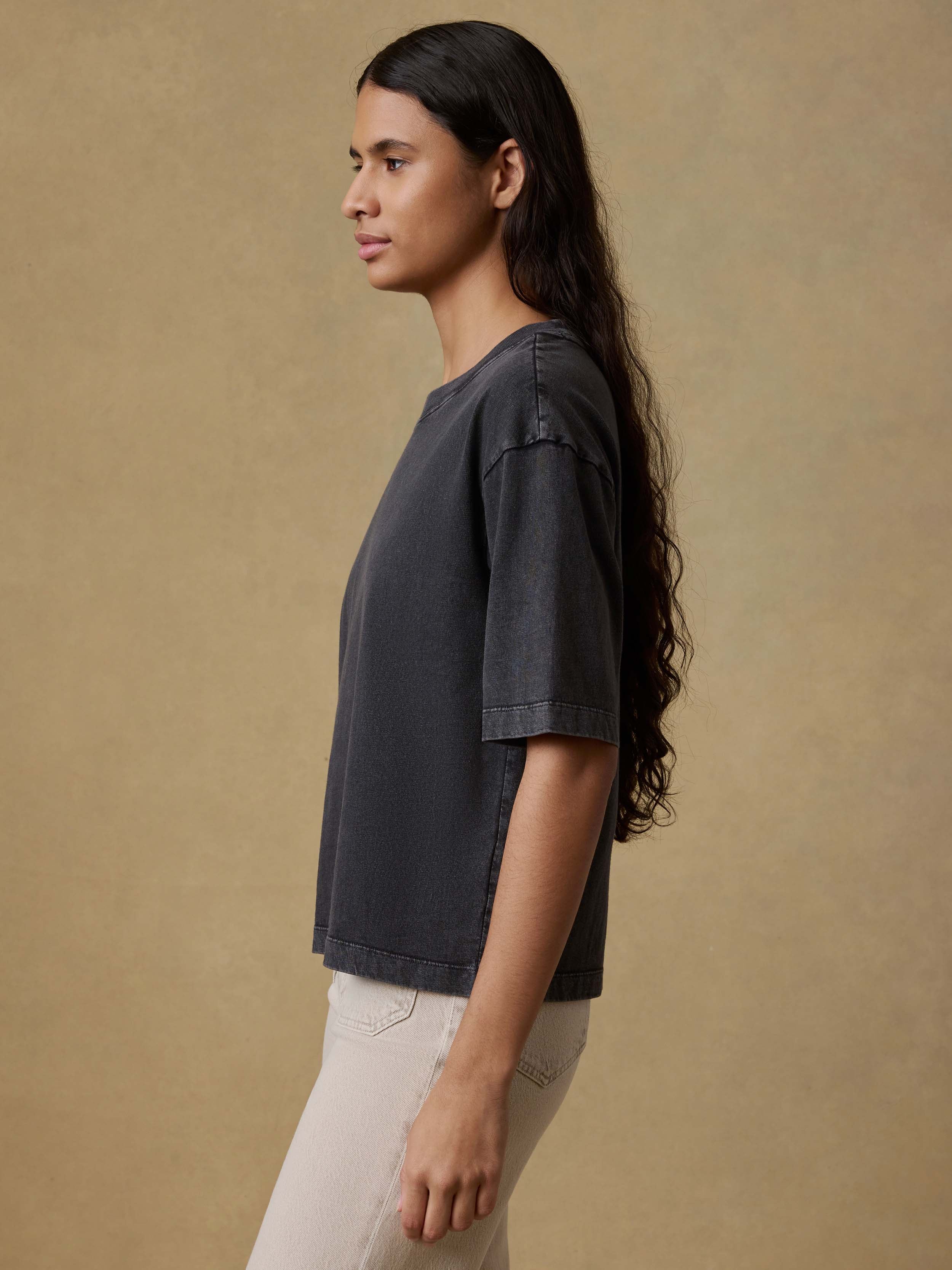 Woman wearing a black t-shirt and beige pants against a brown background