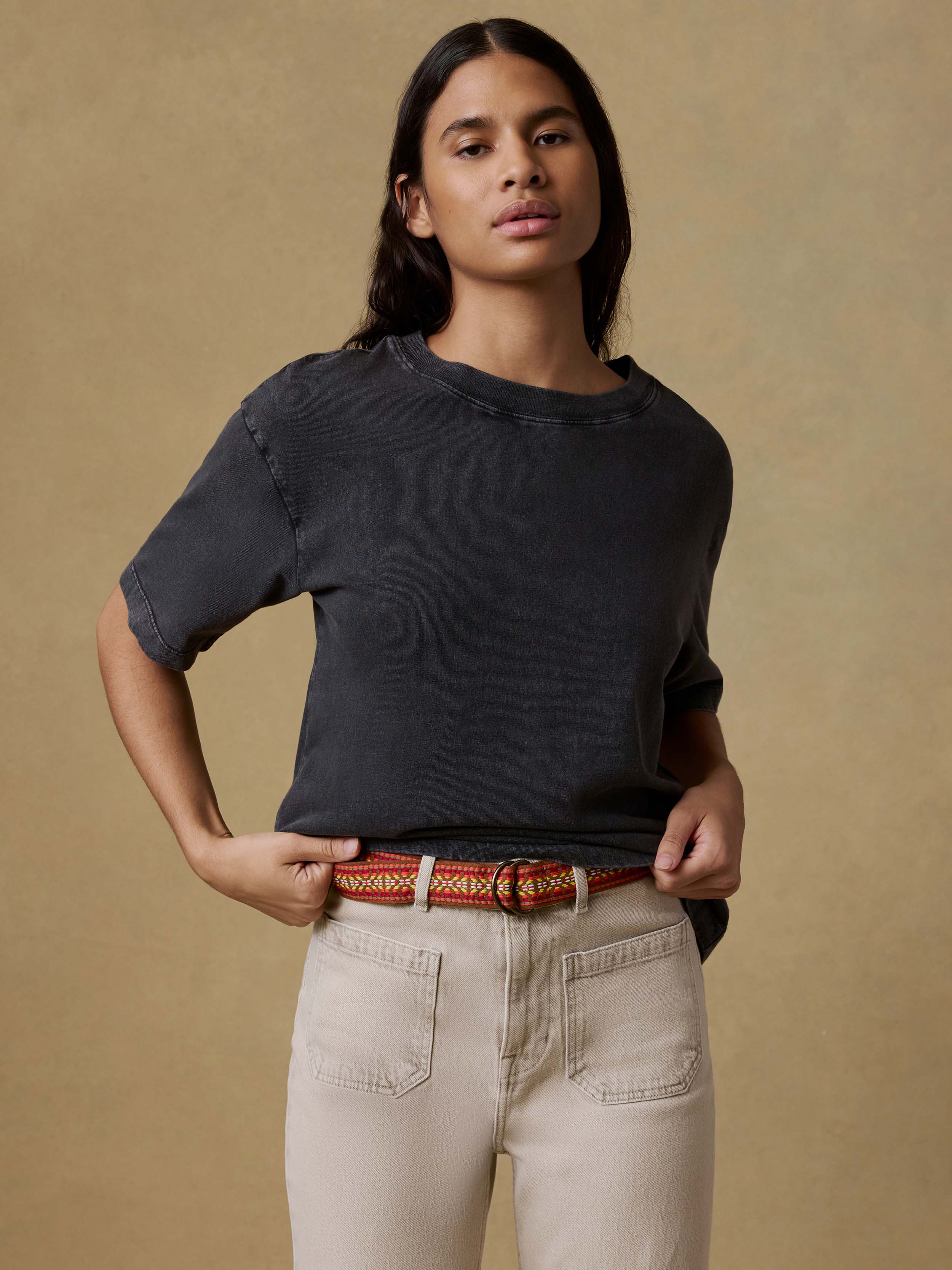 Woman wearing a black t-shirt and beige pants against a brown background