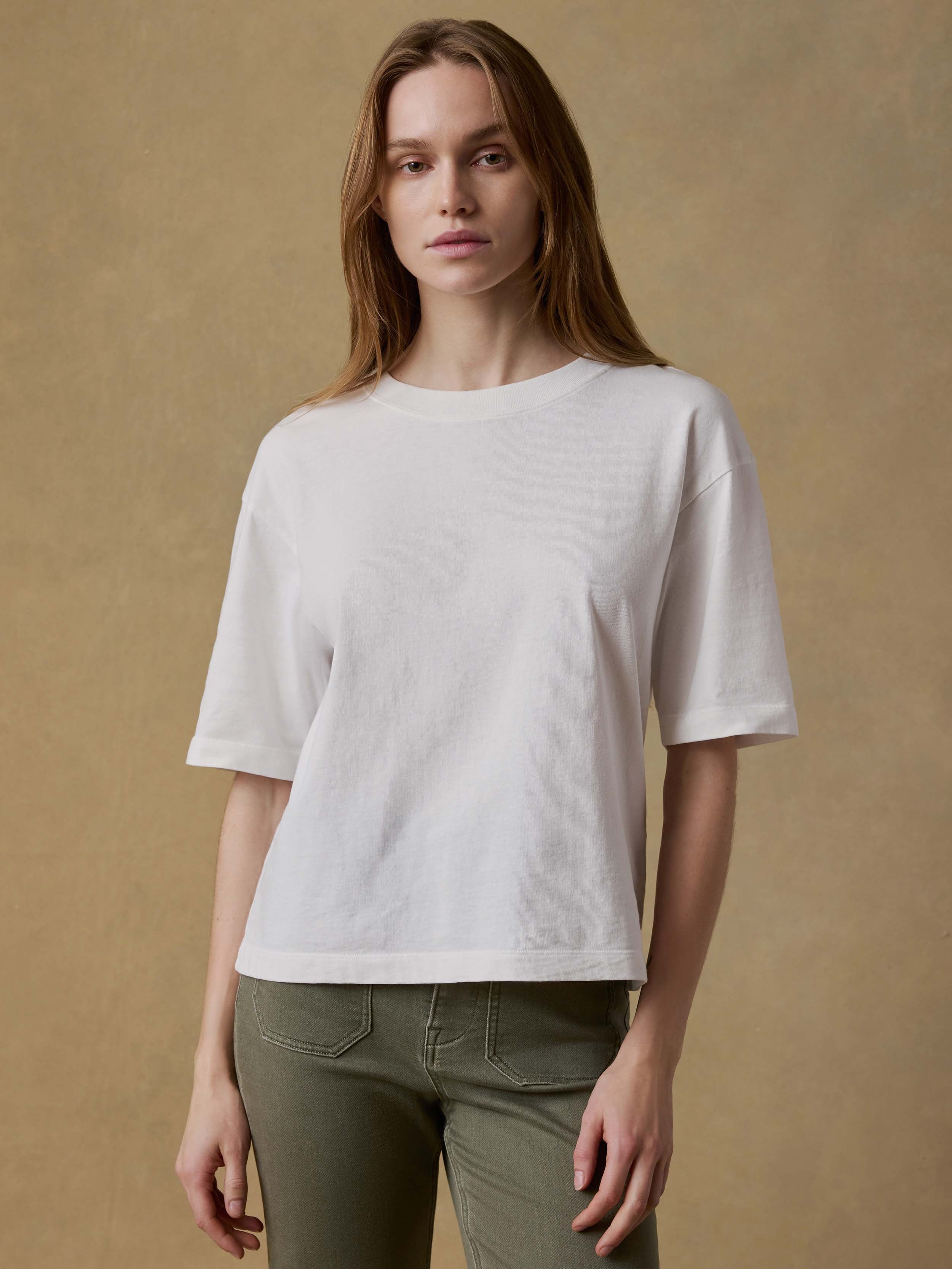 Woman wearing a white t-shirt and green pants against a beige background