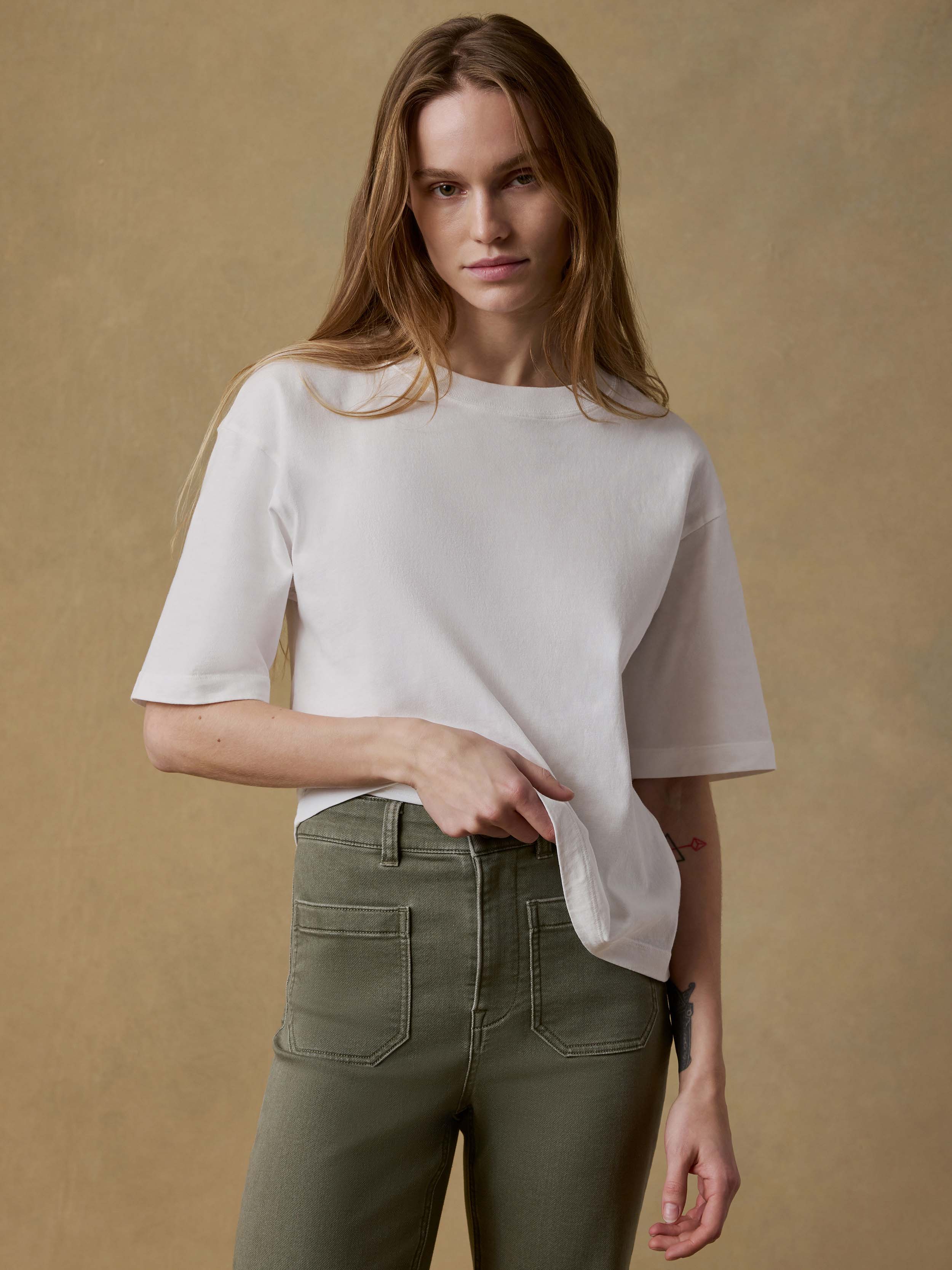 Woman wearing a white t-shirt and green pants against a beige background