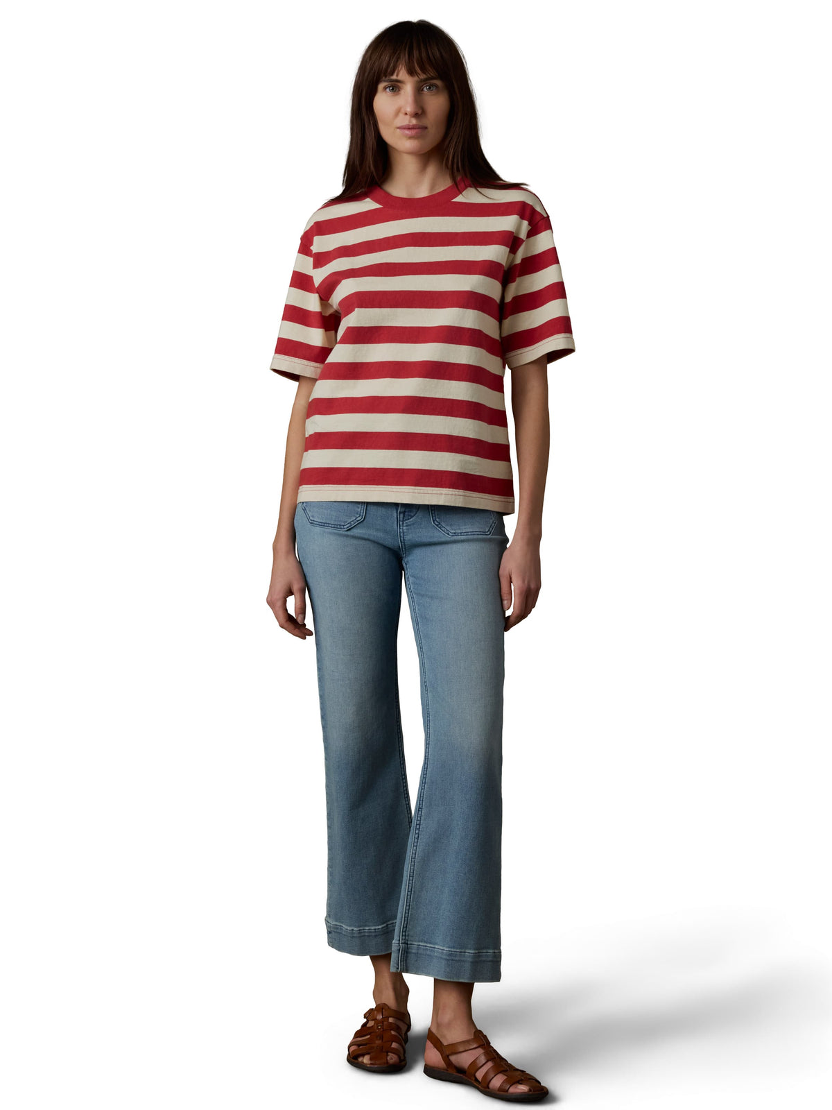 A woman wearing a red and white short sleeve tee, blue jeans, and brown sandals, image 2 of 3