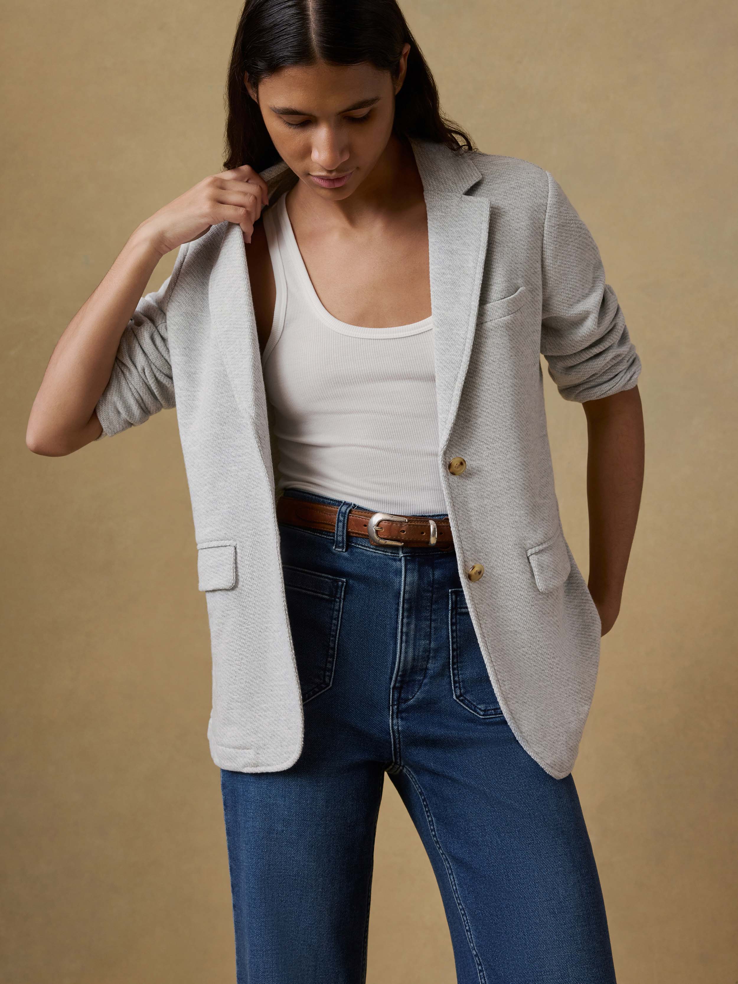 Woman wearing a light gray blazer over a white top and blue jeans on a beige background