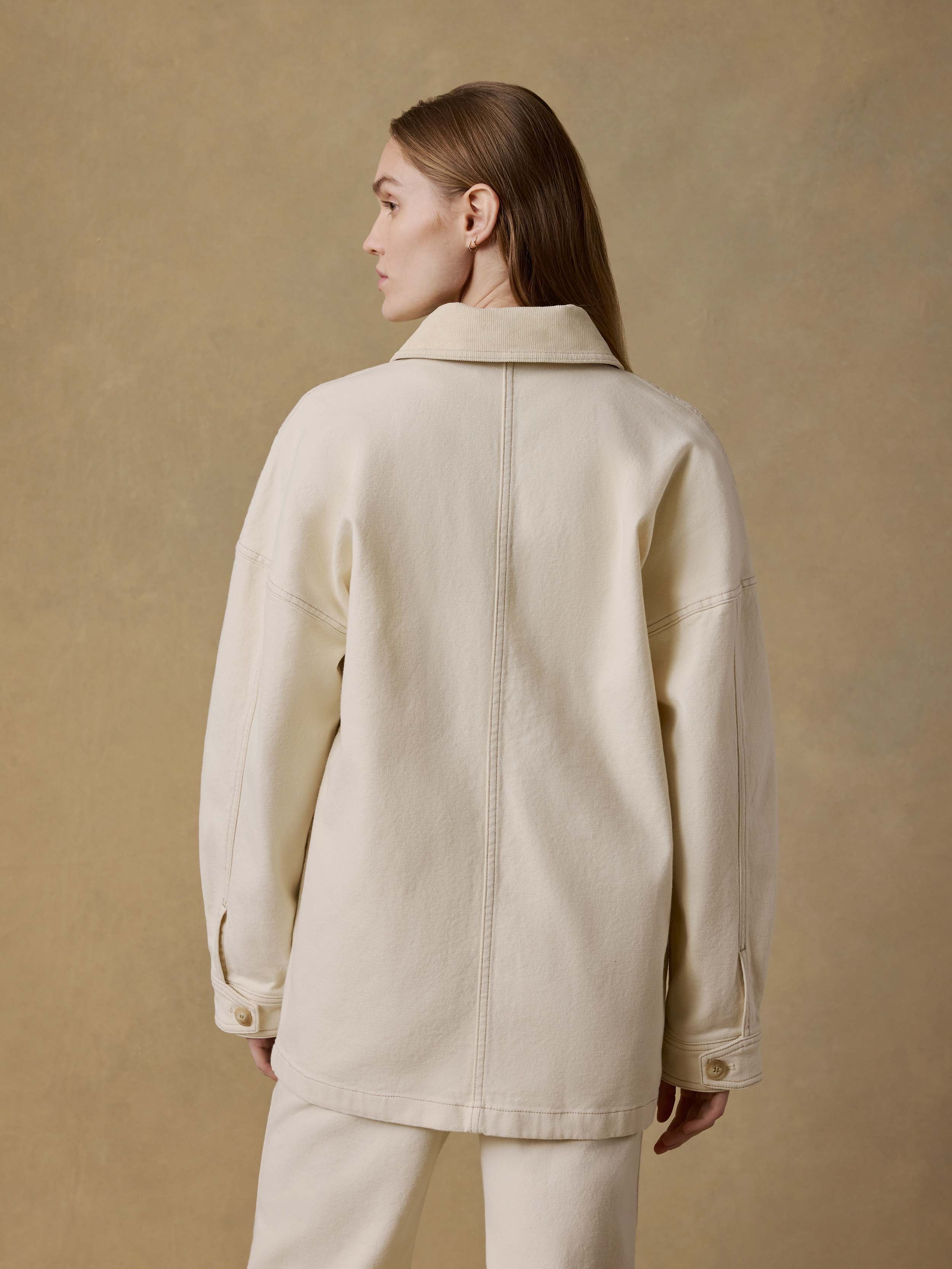 Back view of a woman wearing a light-colored jacket and matching pants against a beige background