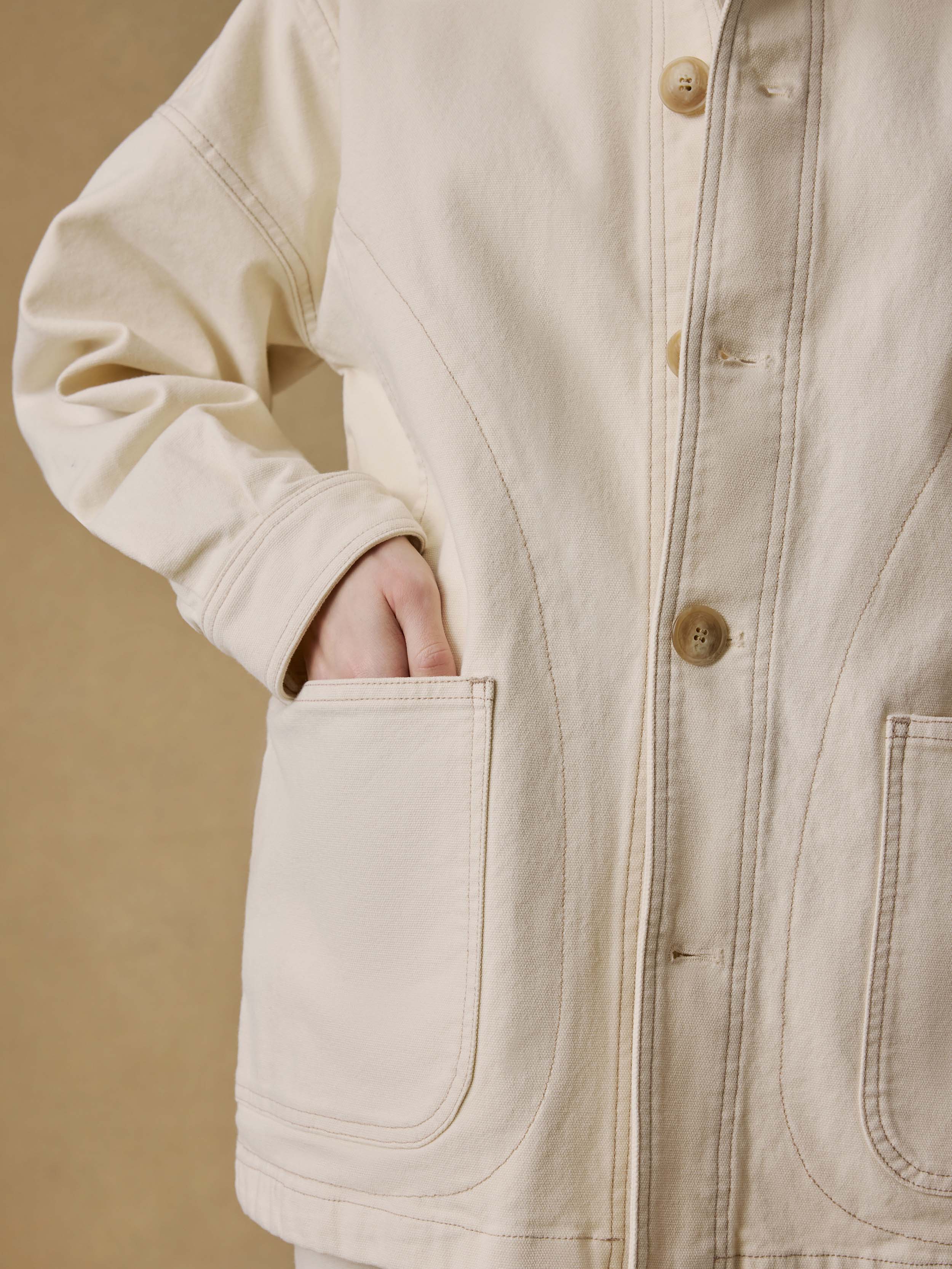 Close-up of a woman wearing a light-colored jacket against a beige background