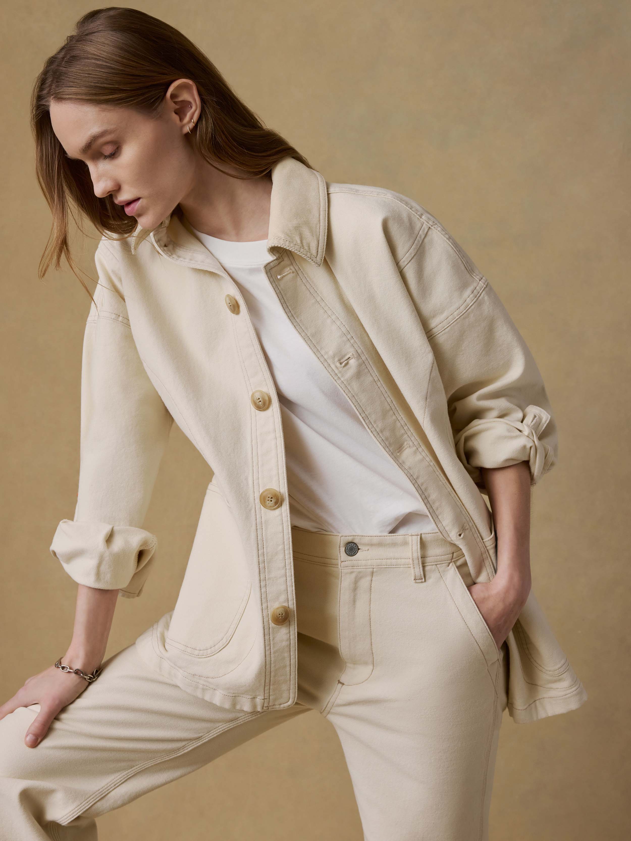 Woman wearing a light-colored jacket and matching pants against a beige background