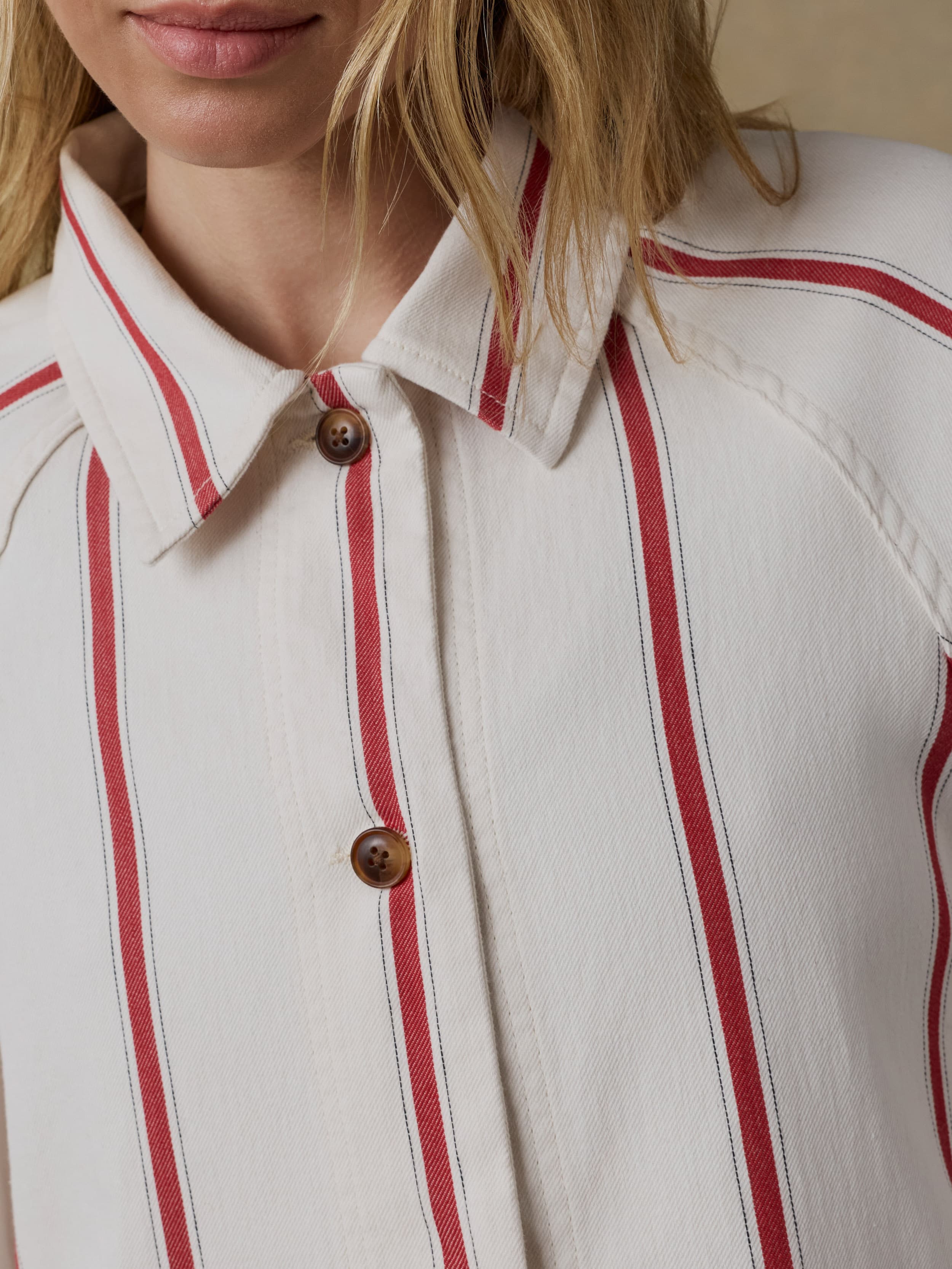 Close-up of a woman wearing a white jacket with red stripes and brown buttons.