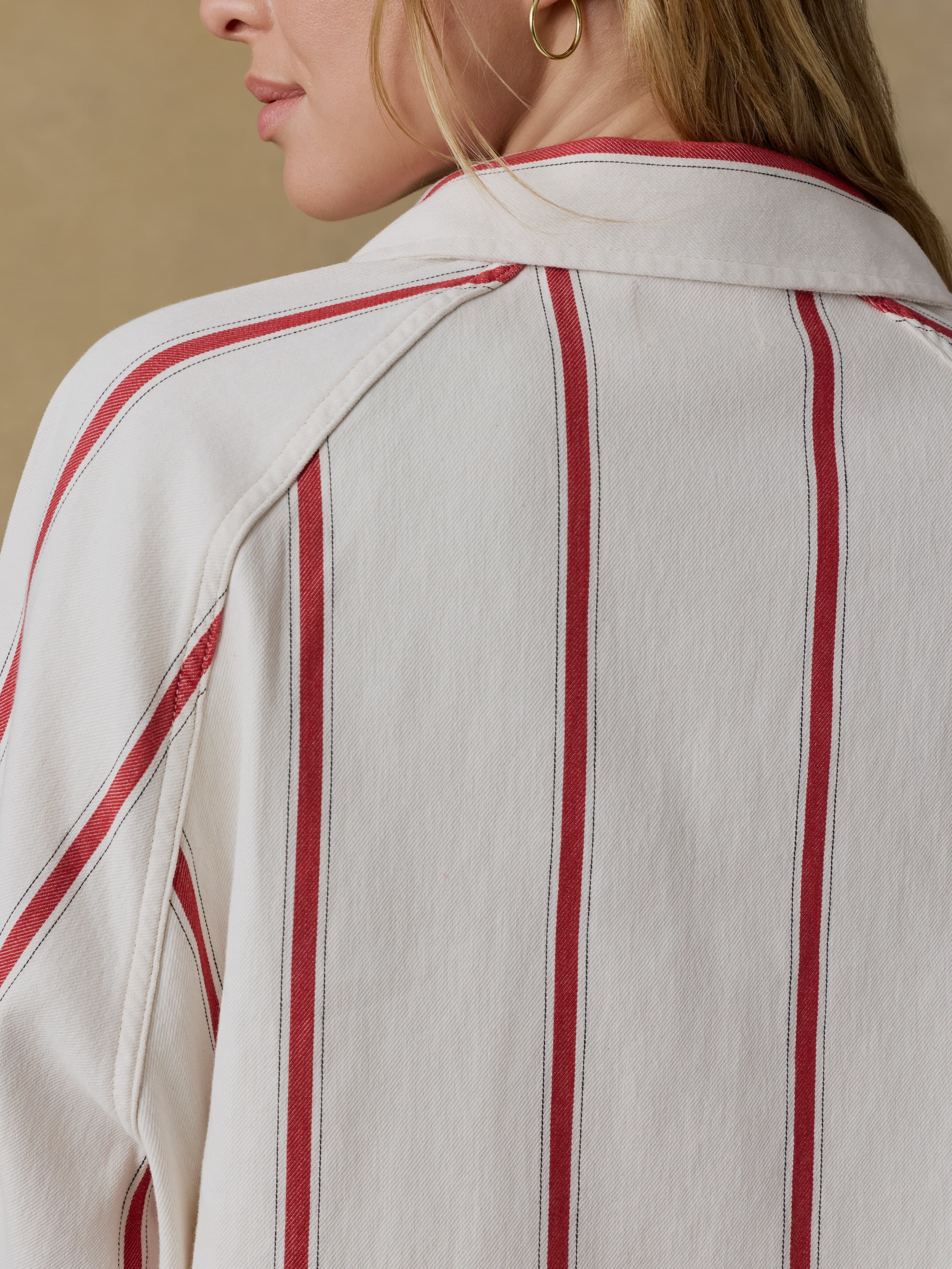 Close-up of a woman wearing a white shirt with red vertical stripes on a beige background