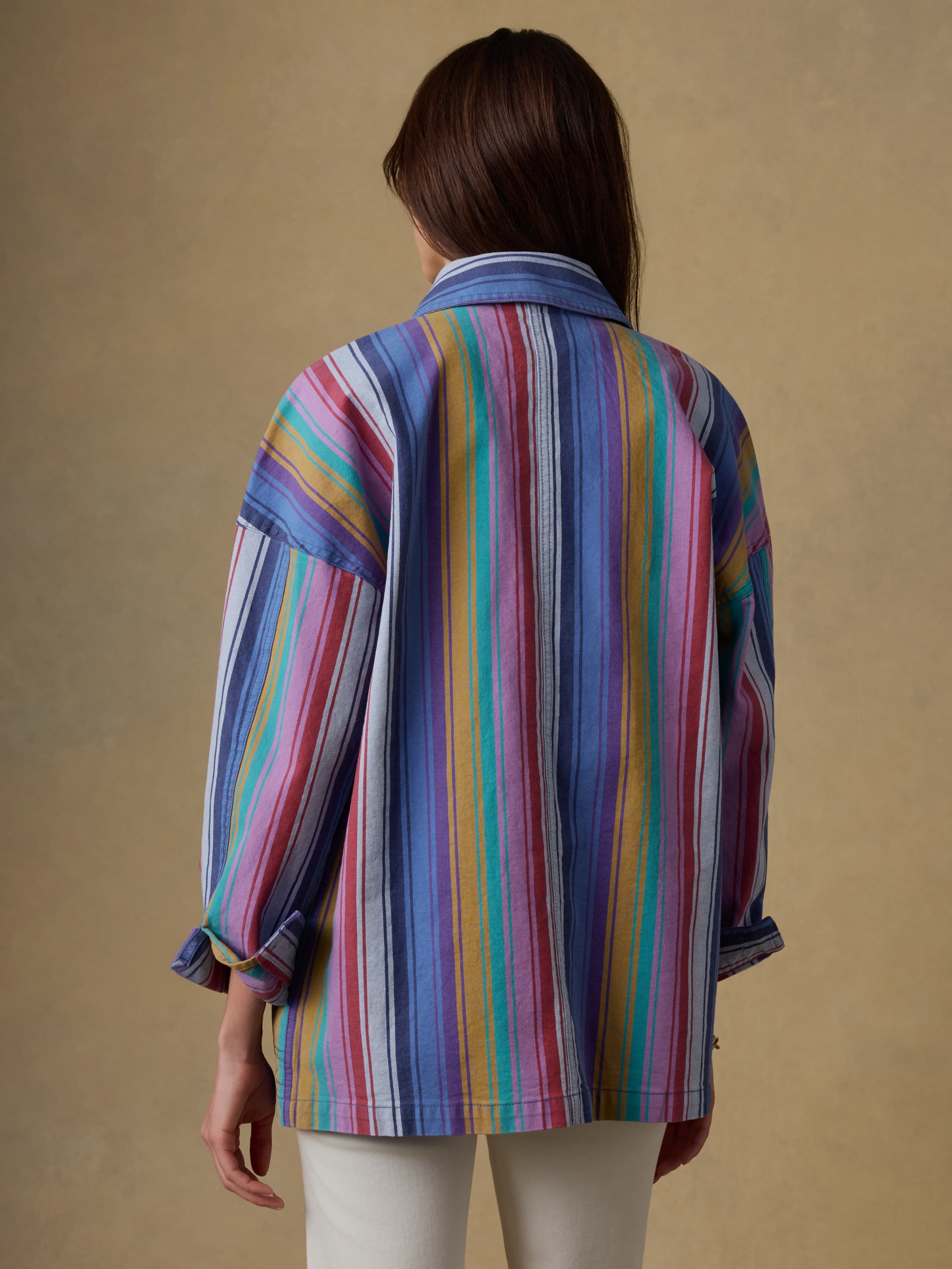 Back view of a woman wearing a colorful striped shirt against a beige background